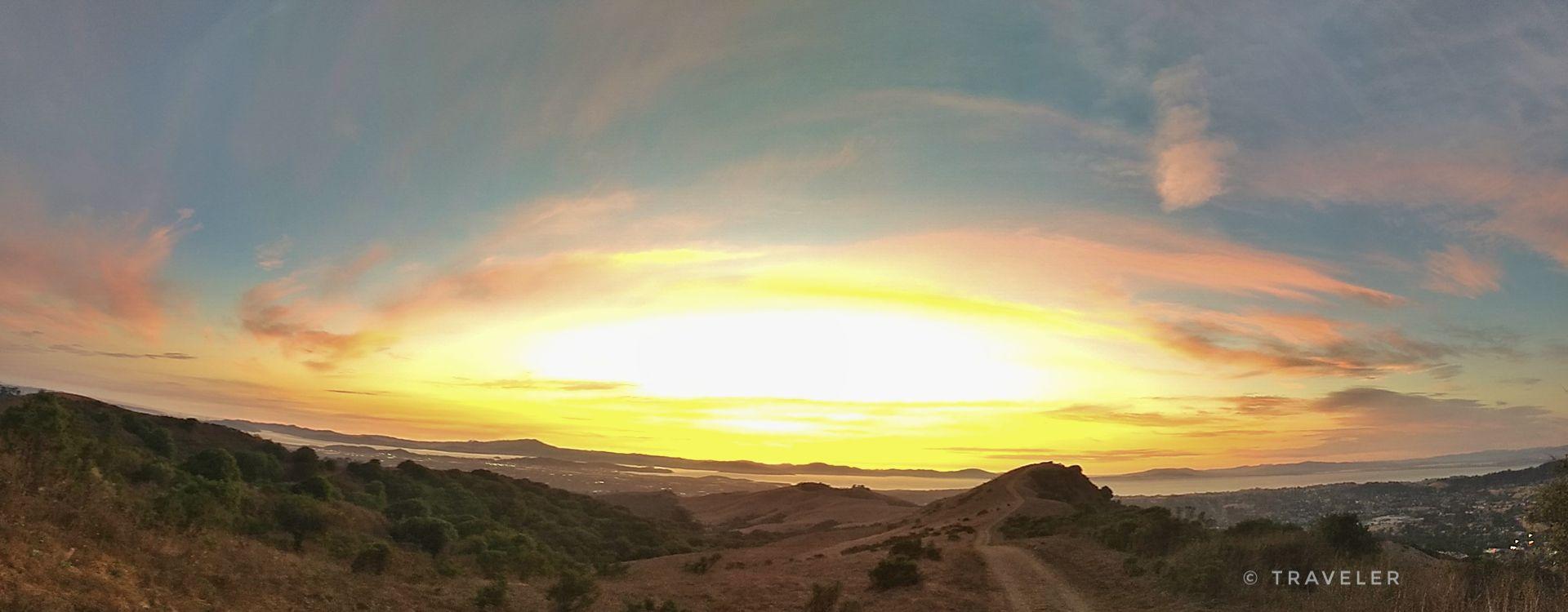 Panoramic view of a vibrant sunset casting warm light over rolling hills.