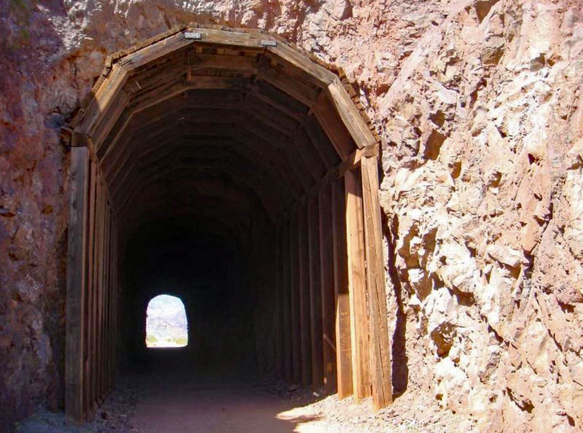 Dark tunnel entrance with wooden framing, light visible at the distant exit. - Railroad Tunnel Trail