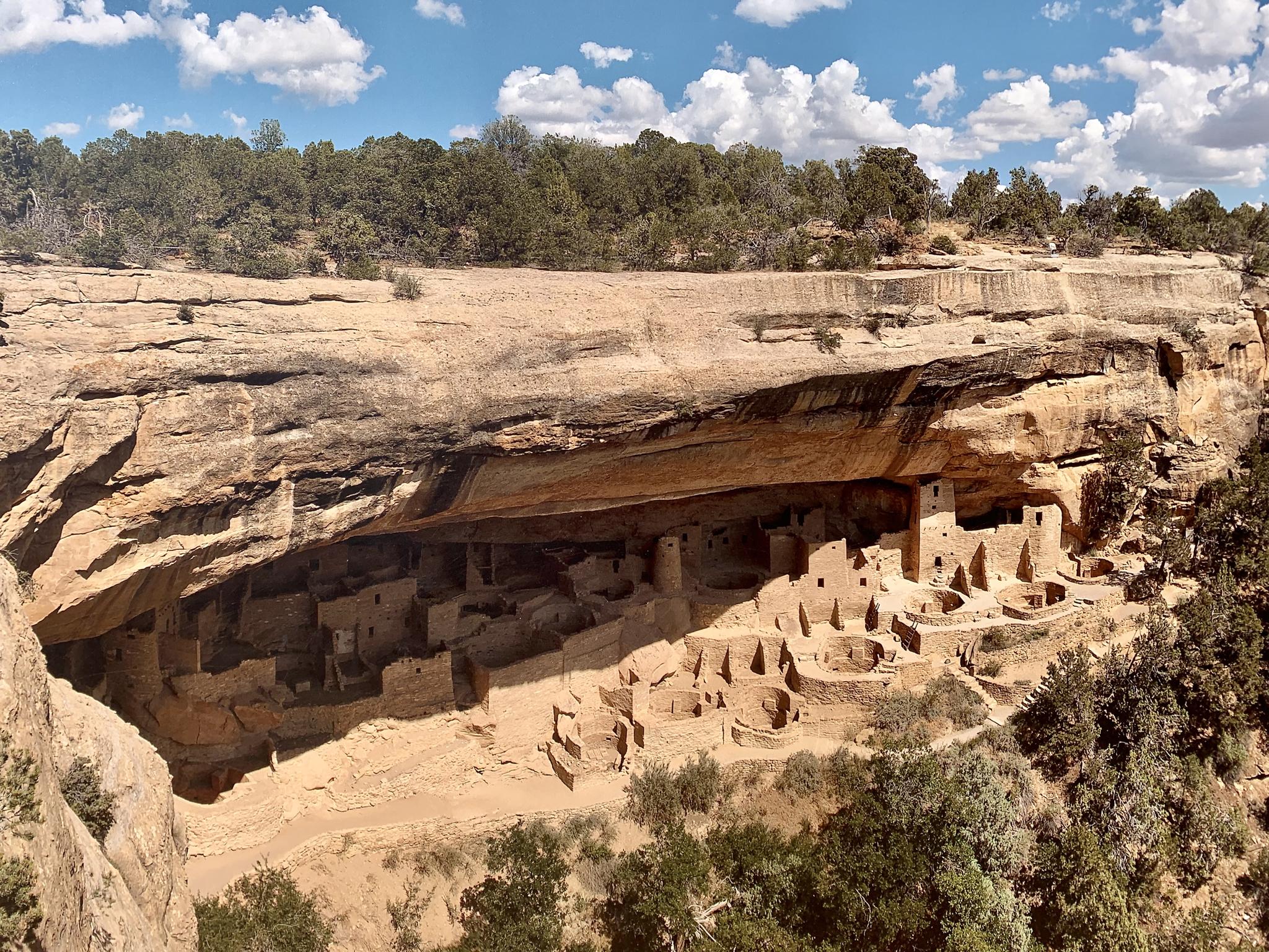 Ancient cliff dwellings built into a large rock overhang under a partly cloudy sky.
