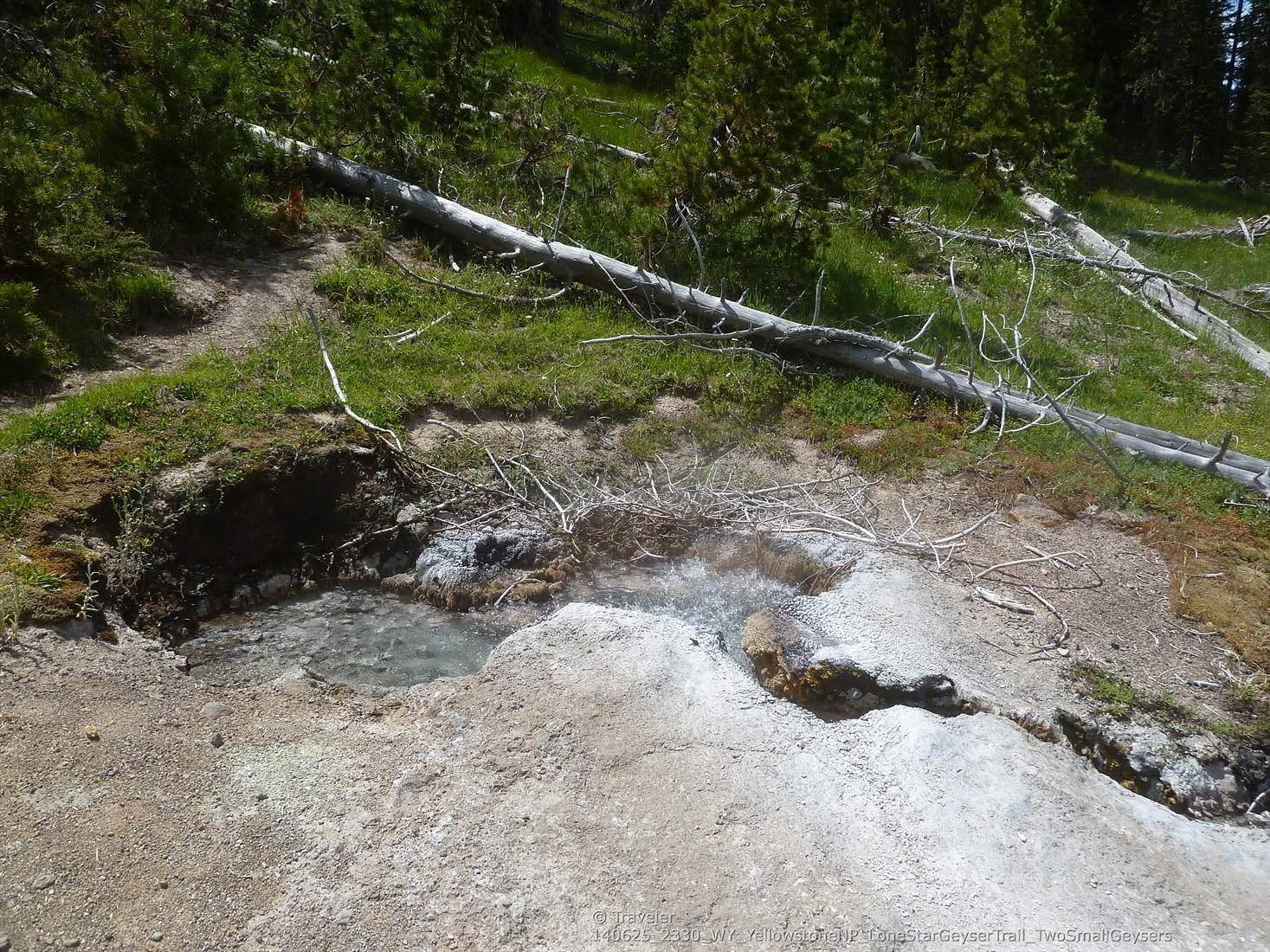 Small steaming hot spring with light blue water, surrounded by dirt and grass.