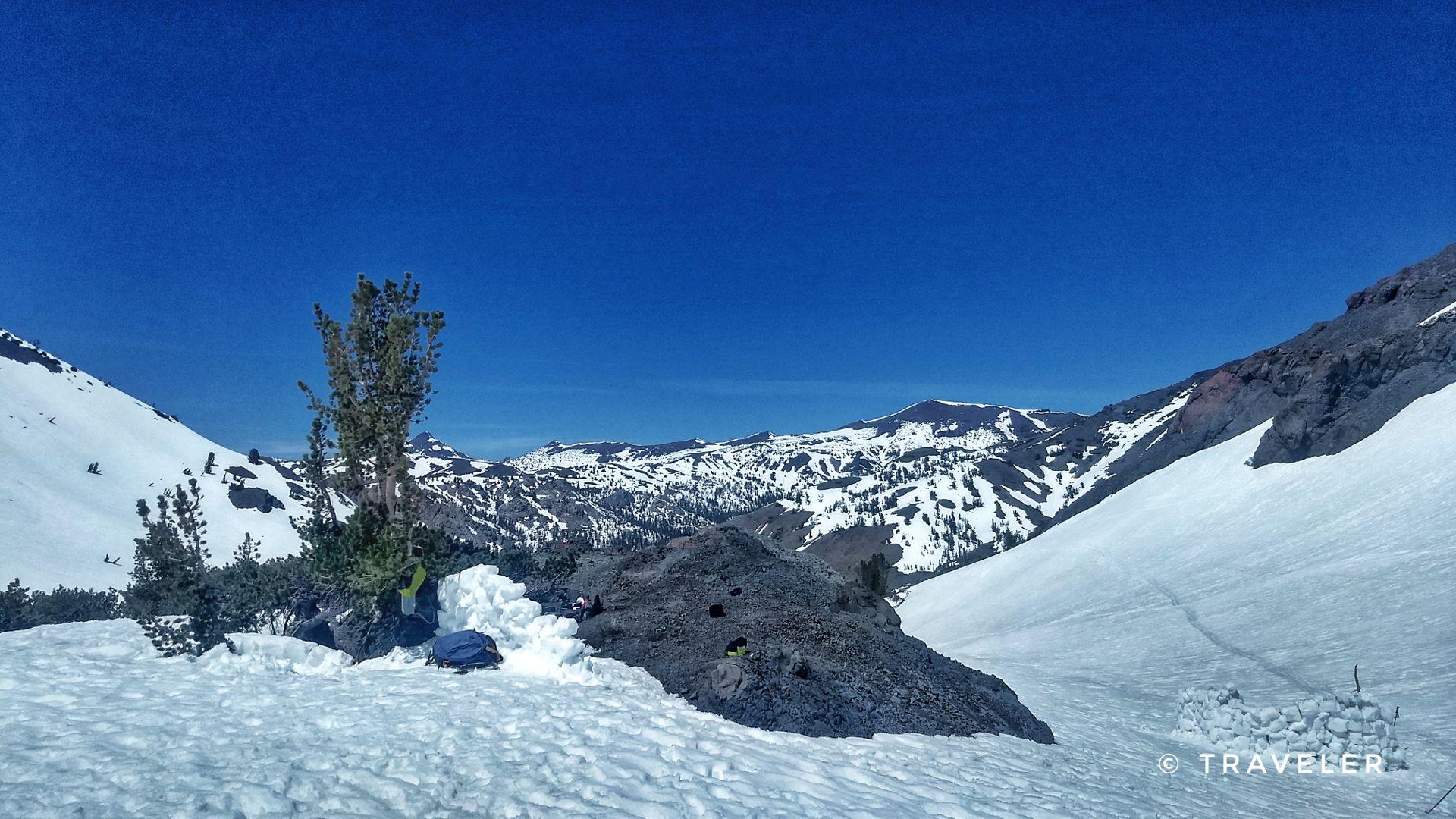 Vast snowy mountain landscape with rocky outcrops under a clear blue sky.