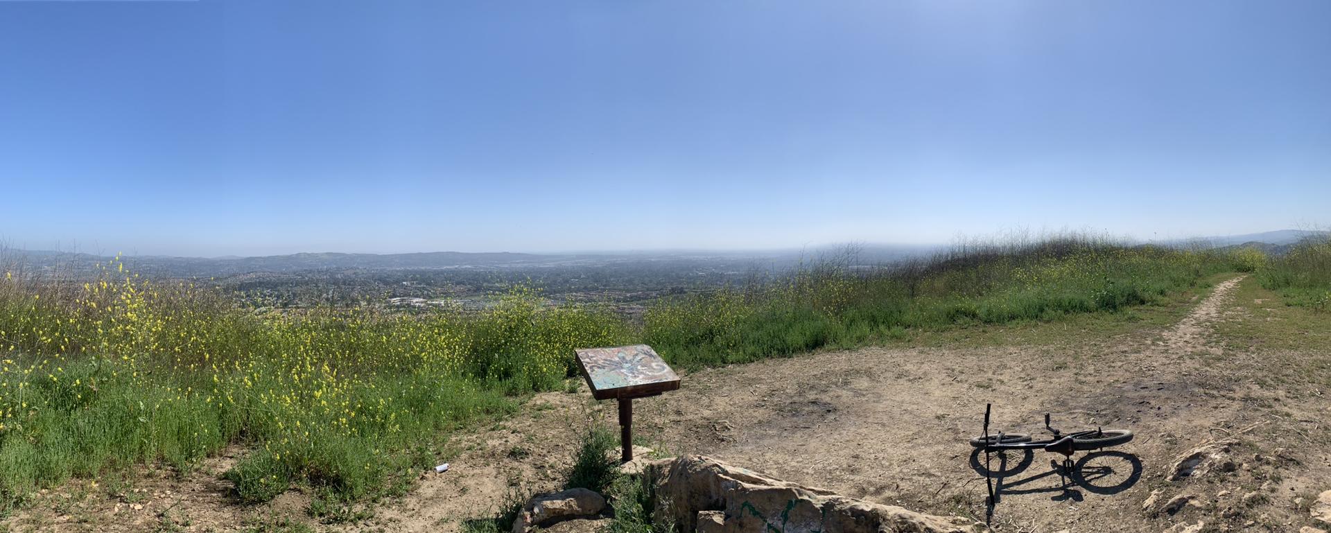 Panoramic view from a hilltop with a bicycle and information sign on a sunny day.