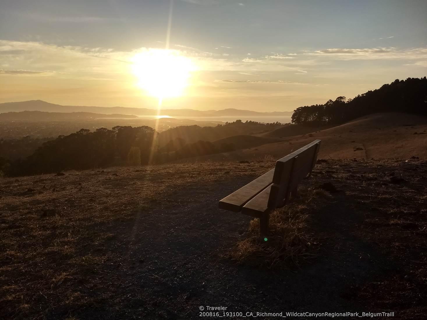 An empty bench overlooks a vast valley during a golden sunset.