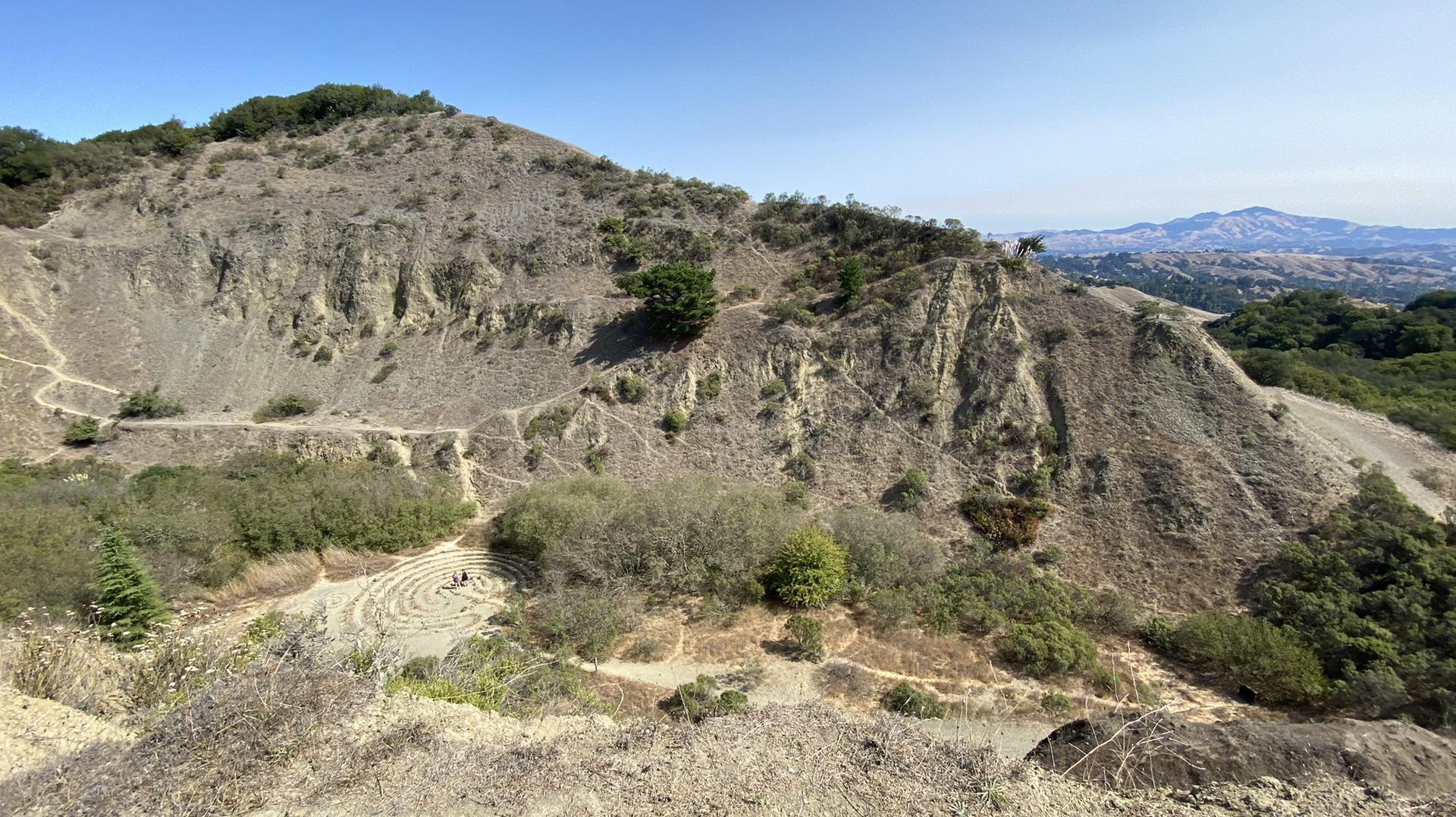 Arid, rocky hills with winding trails and a labyrinth pattern below.