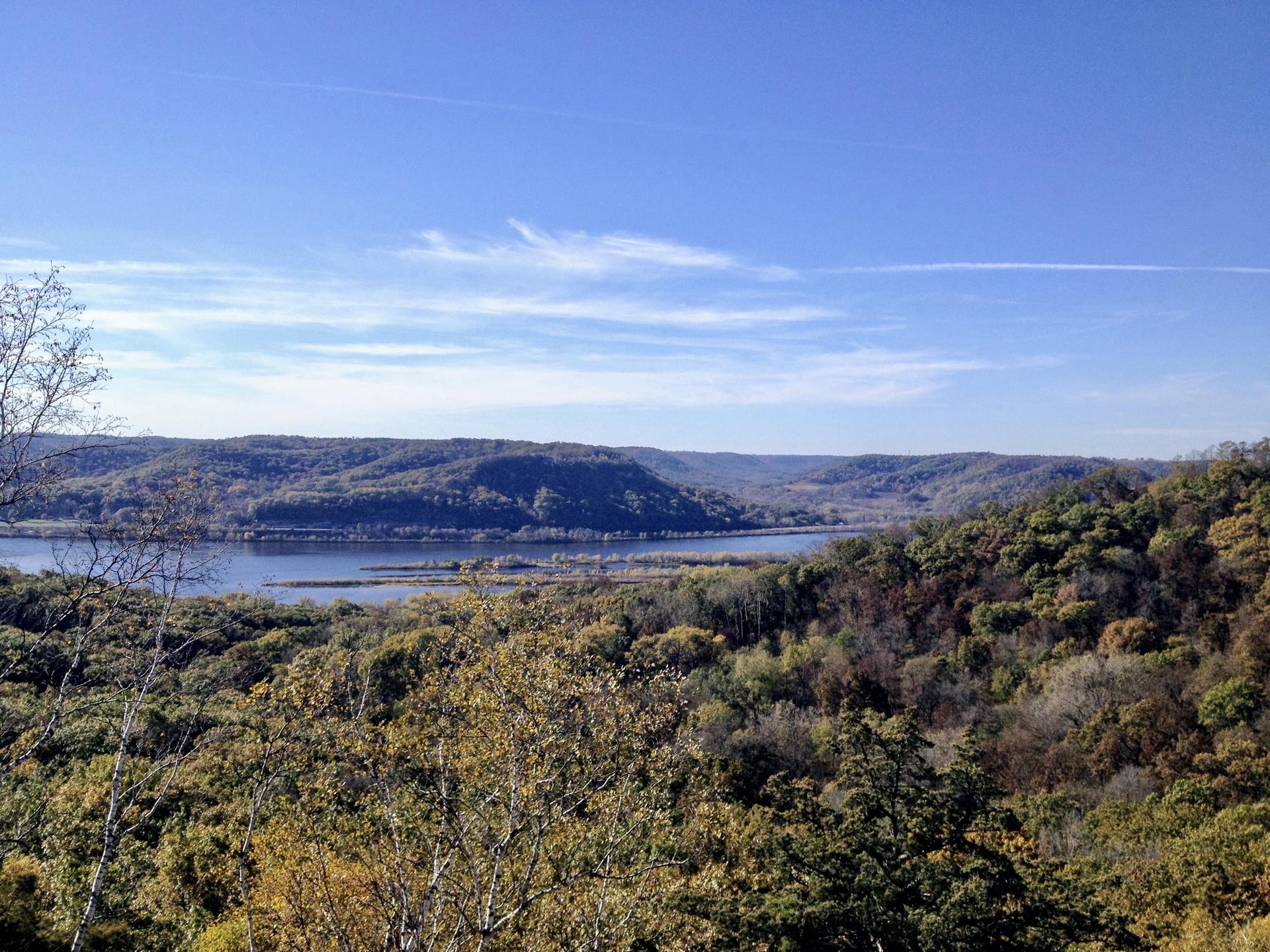 Distant river surrounded by hills with autumn trees under a clear blue sky.