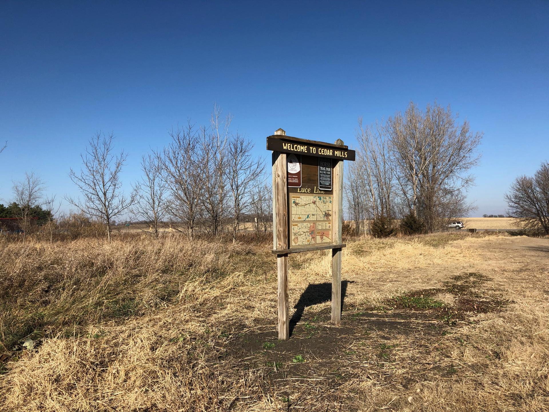 Wooden information sign in a dry grassy field under clear sky.