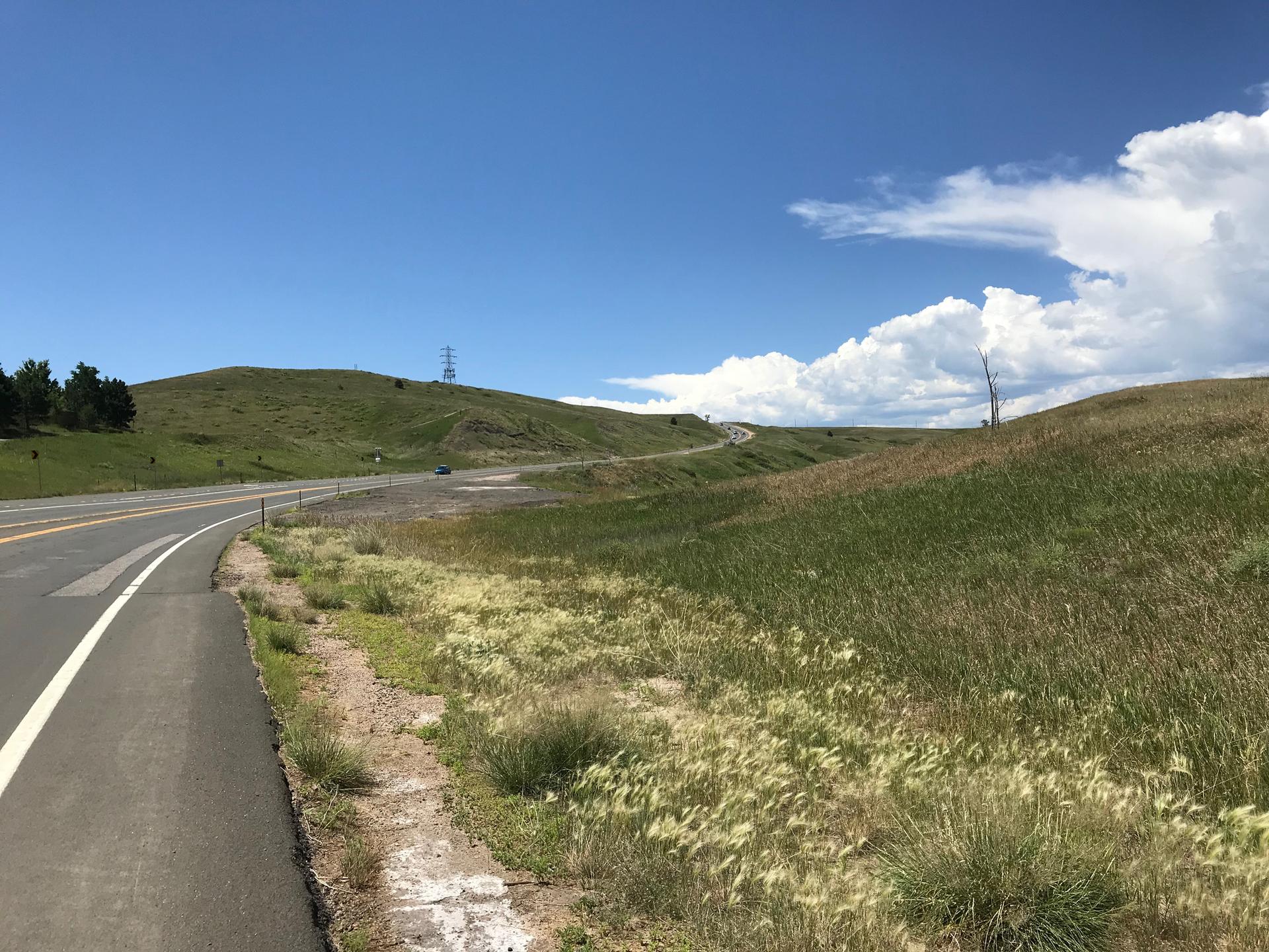 A winding road through green, grassy hills under a bright, cloudy sky.