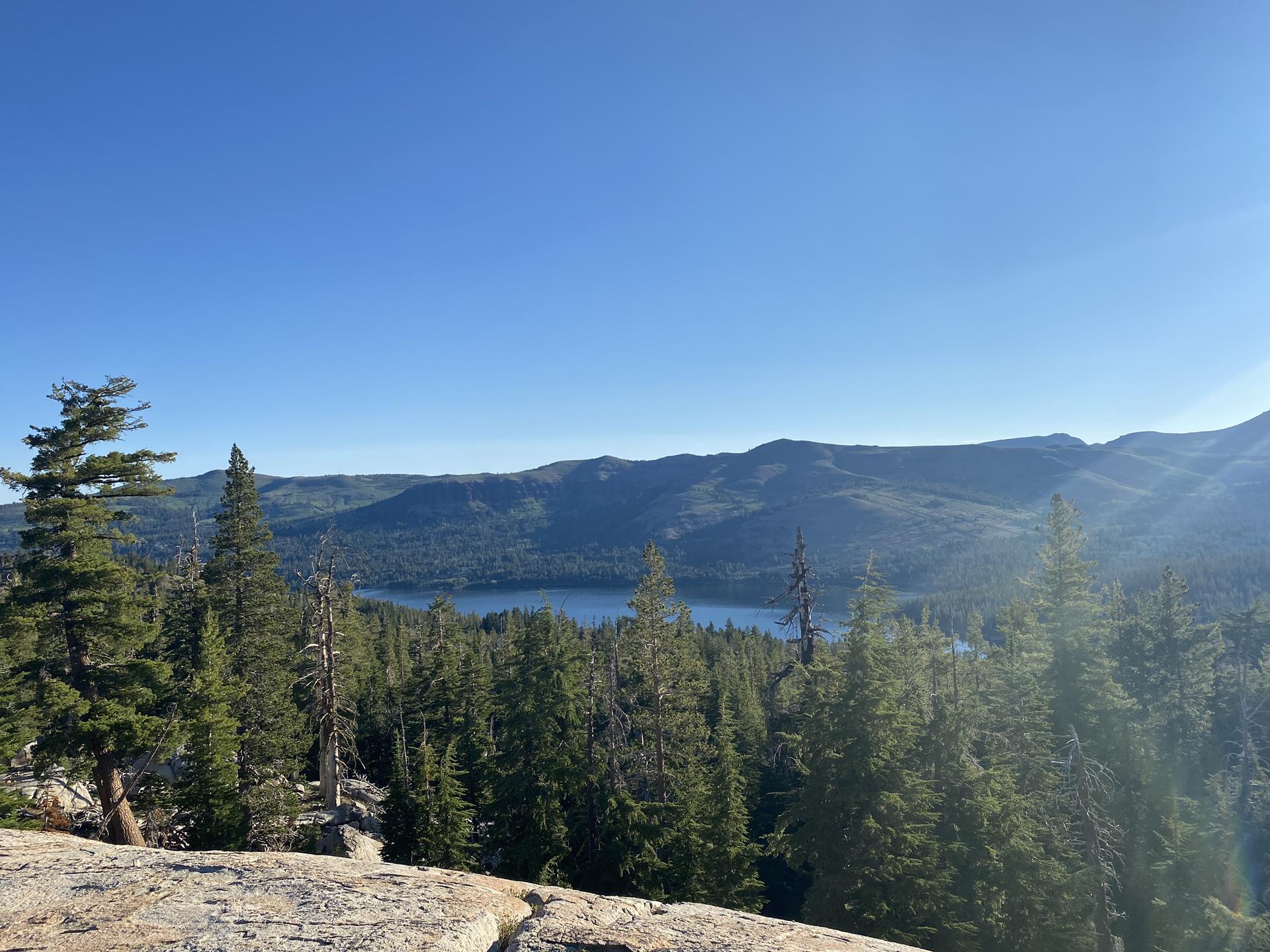 Panoramic view of a serene lake surrounded by dense forest and mountains.