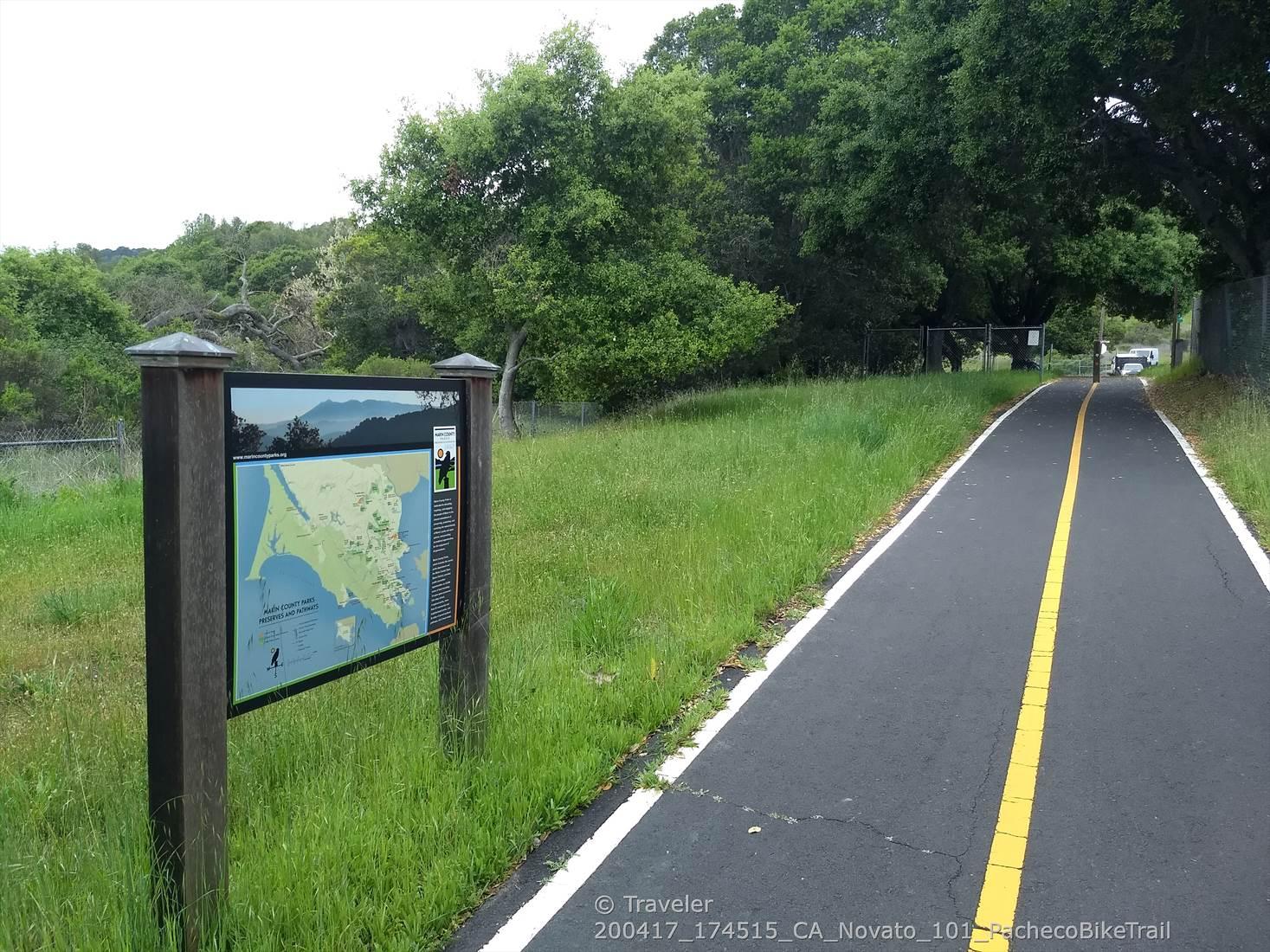 A paved path with a yellow line next to a map display and green grass.