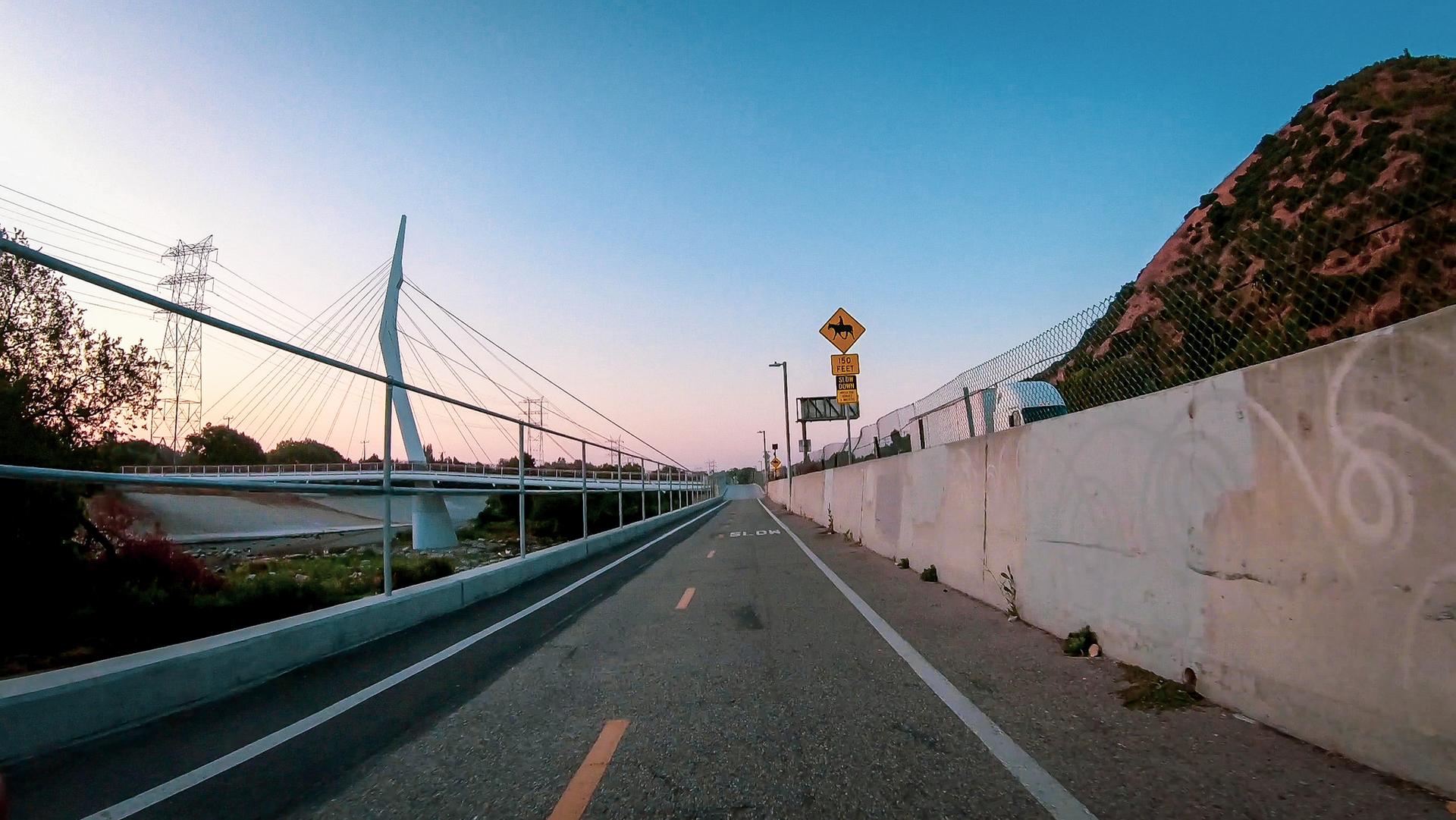 Paved path next to a modern cable-stayed bridge at dusk, soft light.