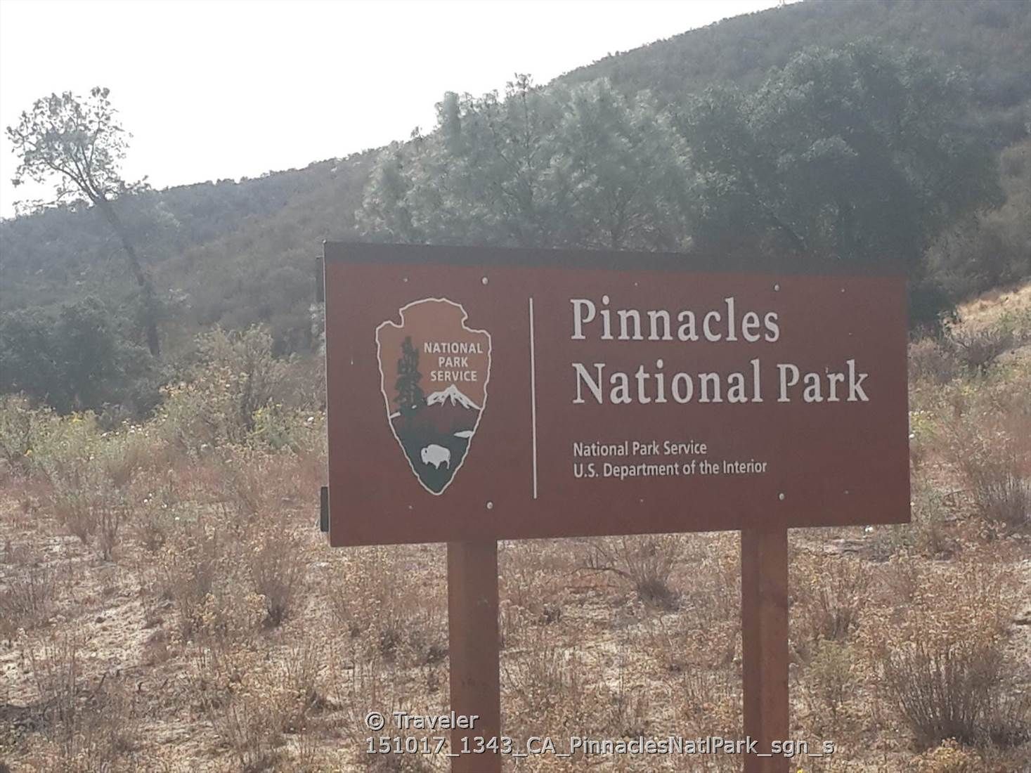 Brown sign on a dry, brushy hillside under bright, hazy sunlight. - Bench Trail