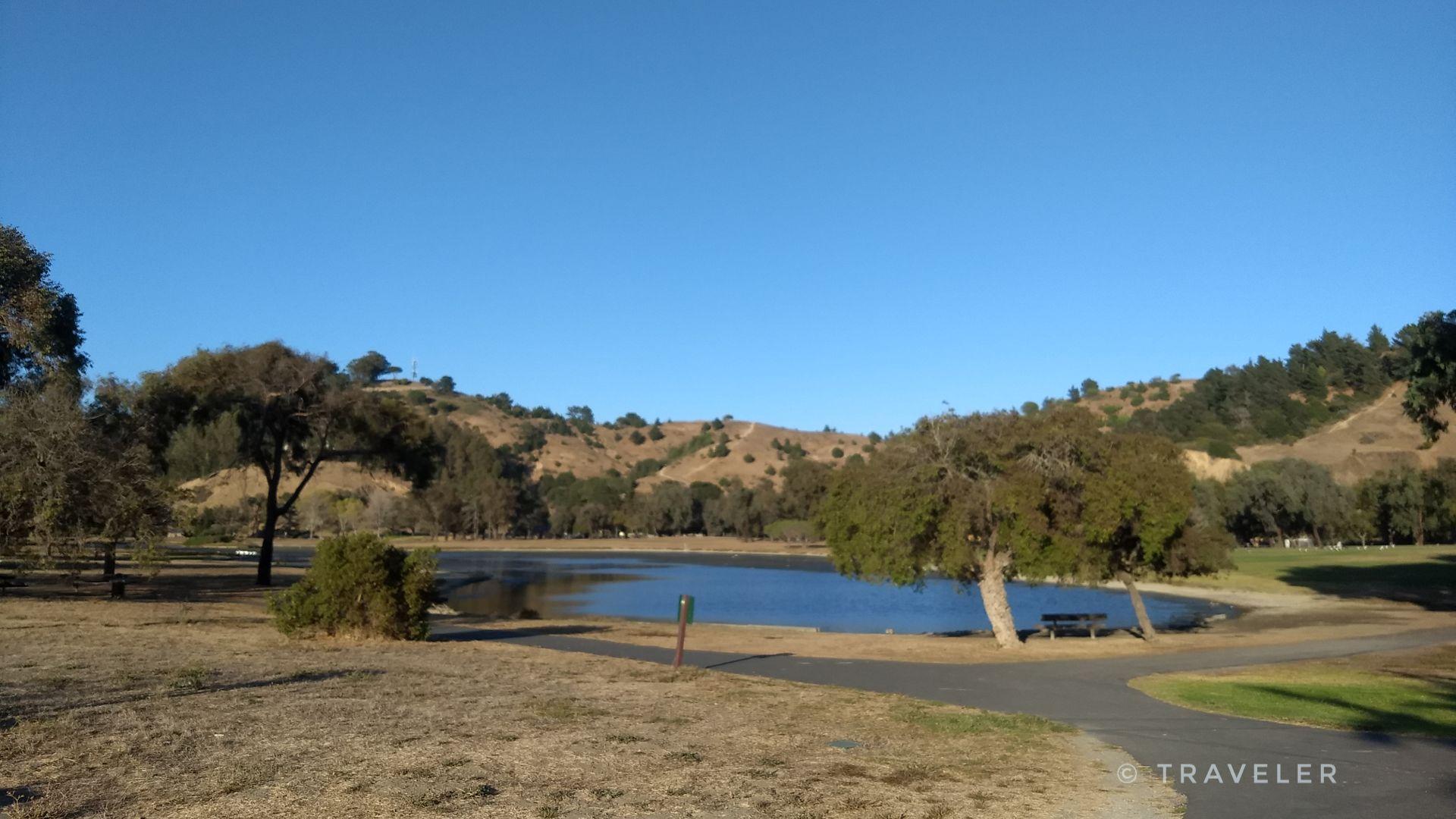 Serene lake surrounded by dry hills and scattered trees under a clear blue sky.