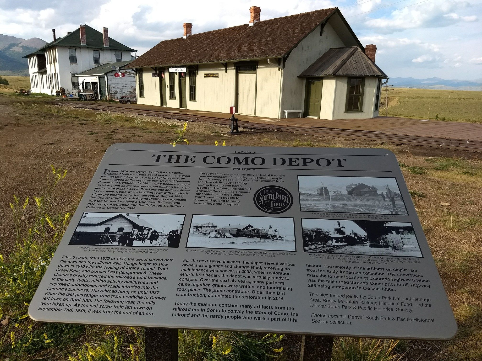 Information sign in foreground with old buildings and railroad tracks behind. - Como — Fairplay