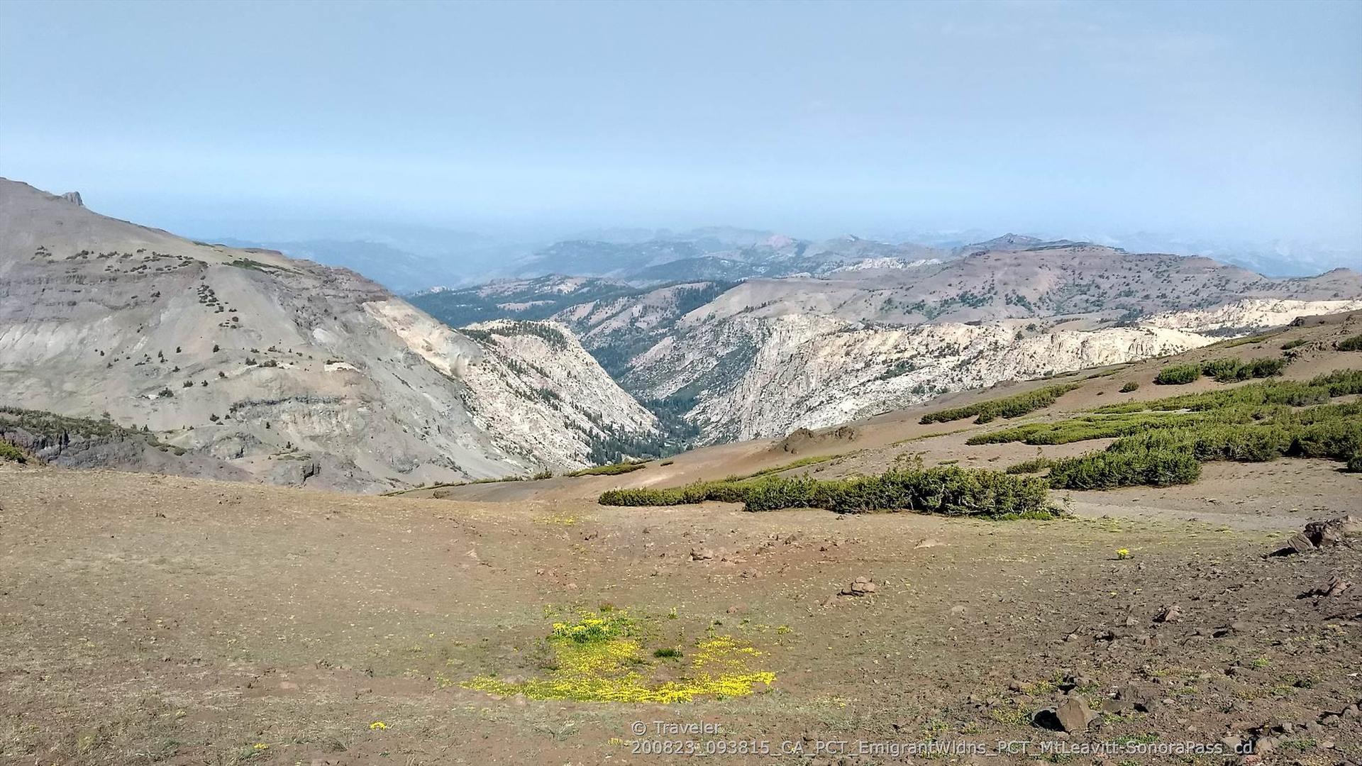 A wide mountain valley with distant peaks and patches of green vegetation.