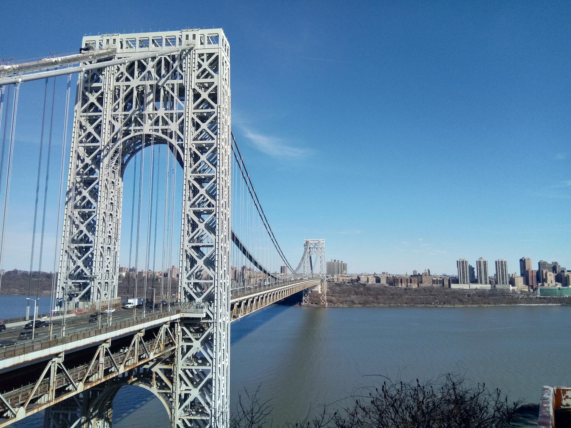 A large suspension bridge tower stands over a wide river under a clear blue sky.