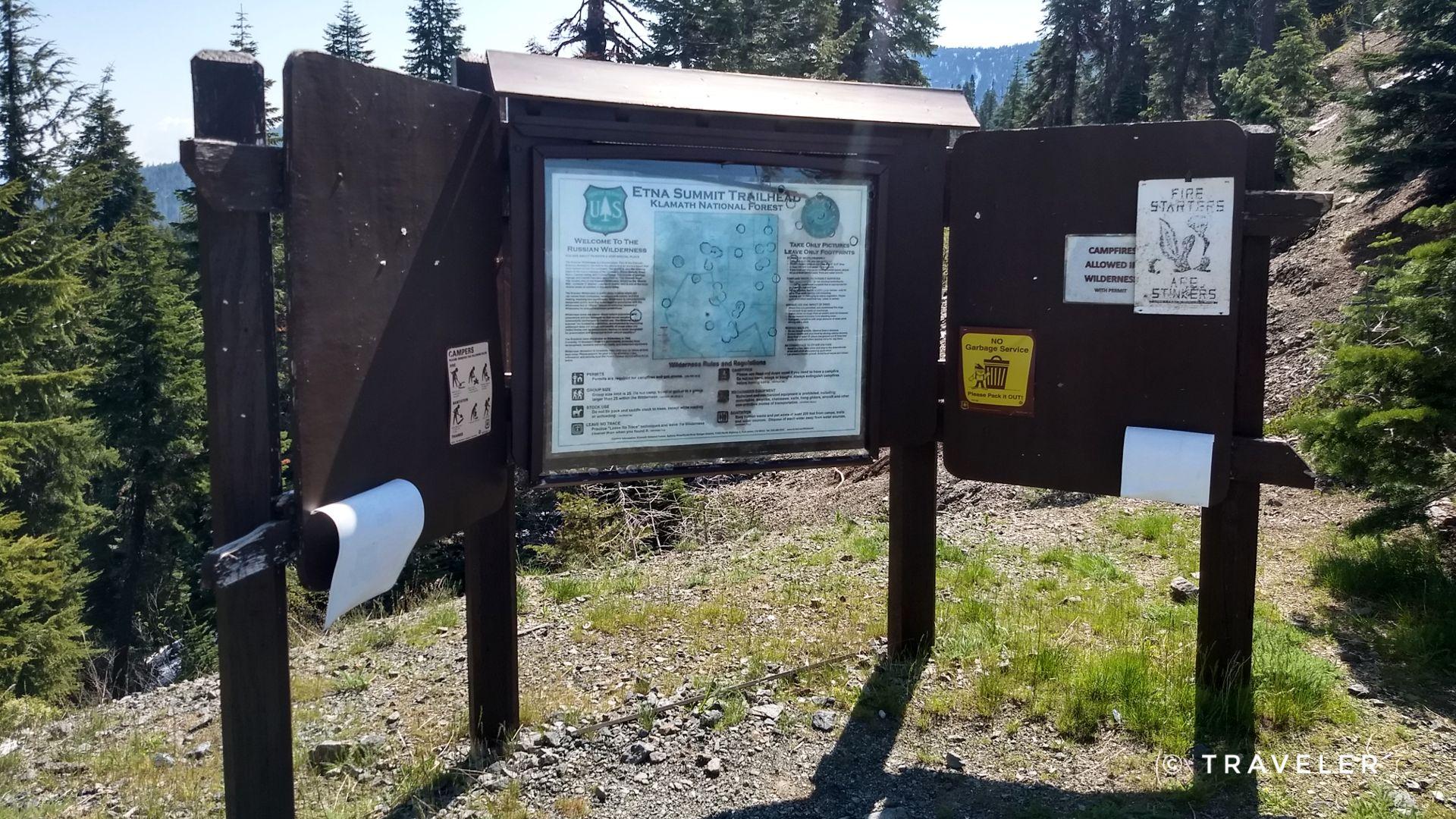 Wooden information board with maps and notices on a sunny day.