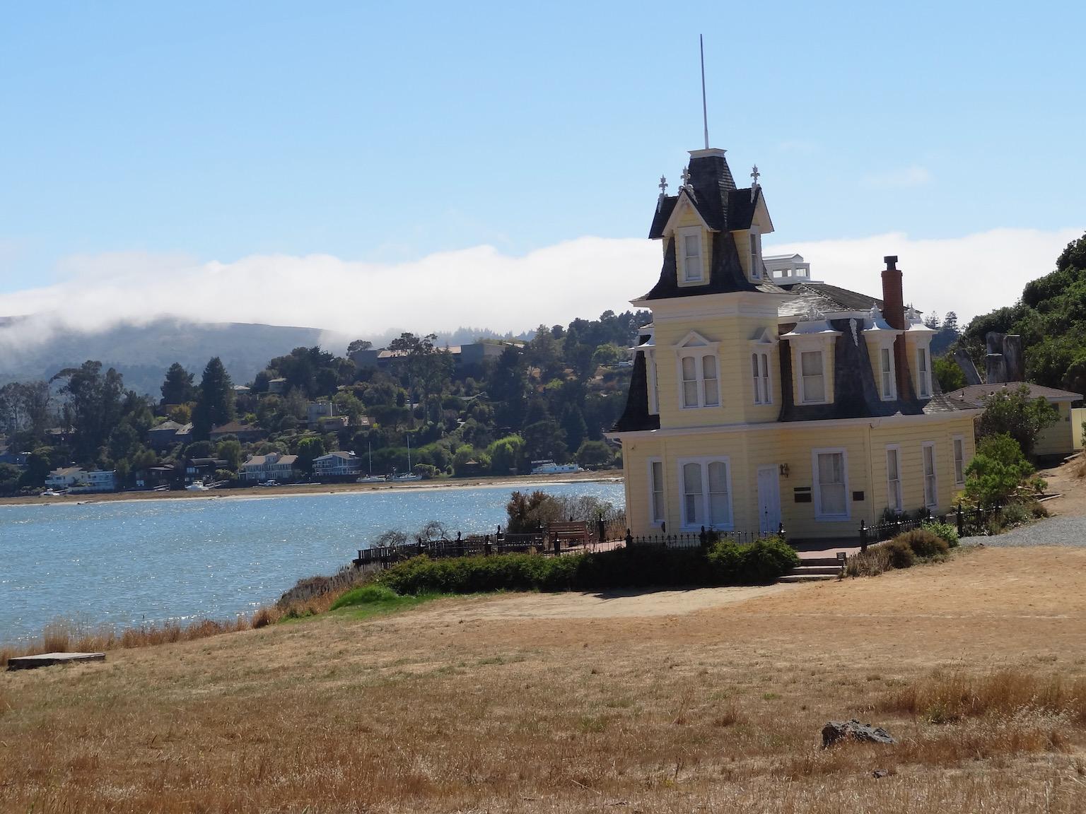 Yellow Victorian house on a dry grassy hill overlooking a bay.
