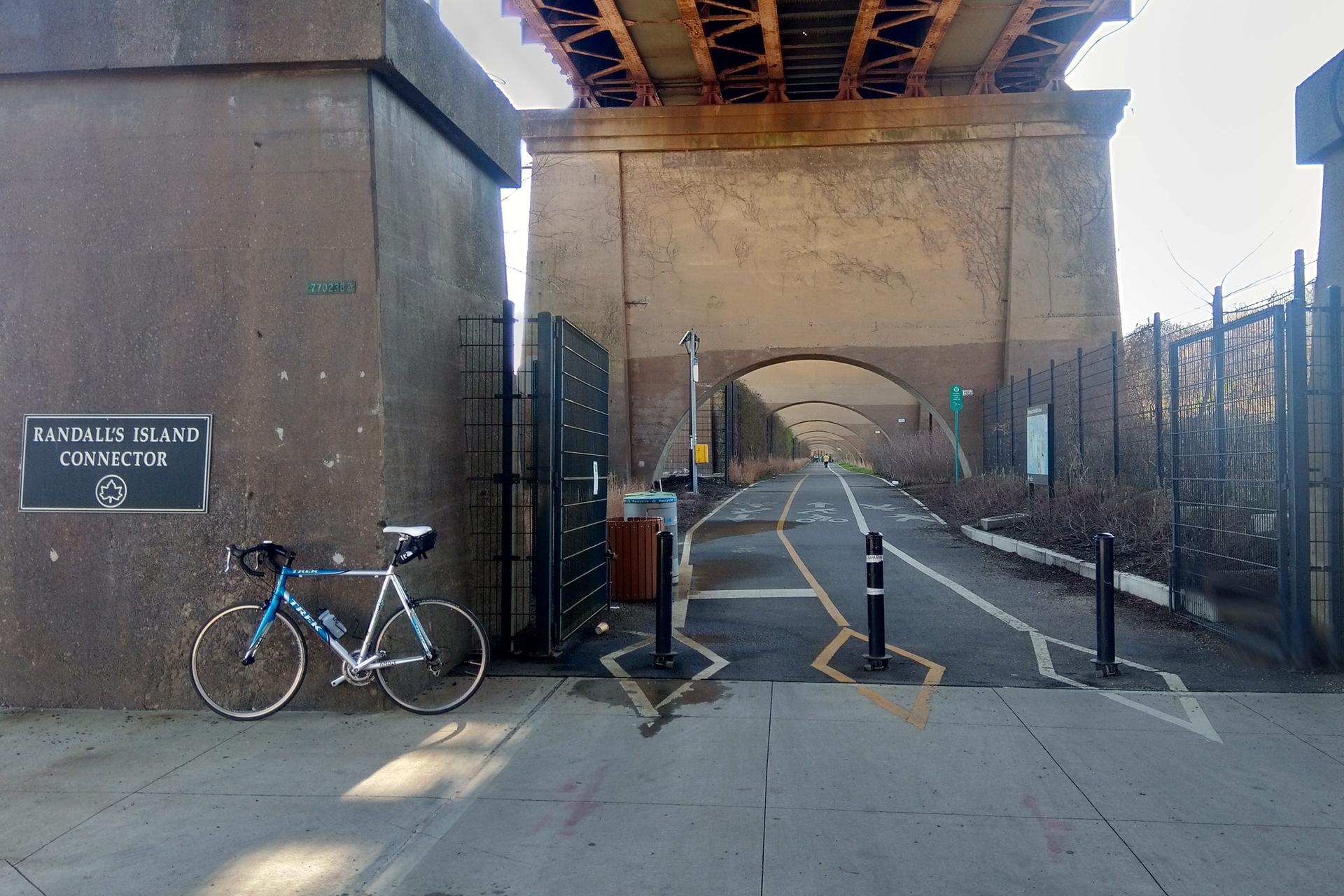 Bicycle parked next to a paved path under a large concrete bridge.