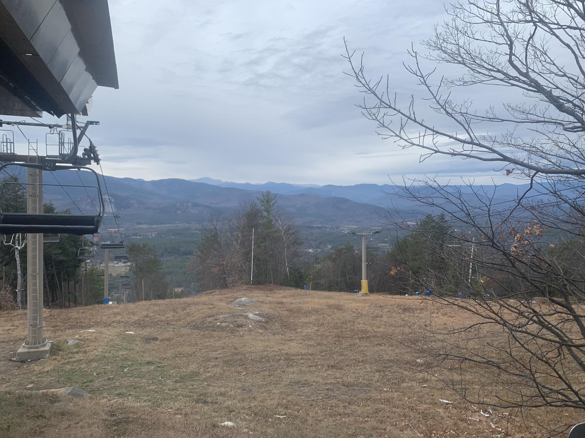Ski lift chair overlooking distant mountains and a grassy slope on a cloudy day.
