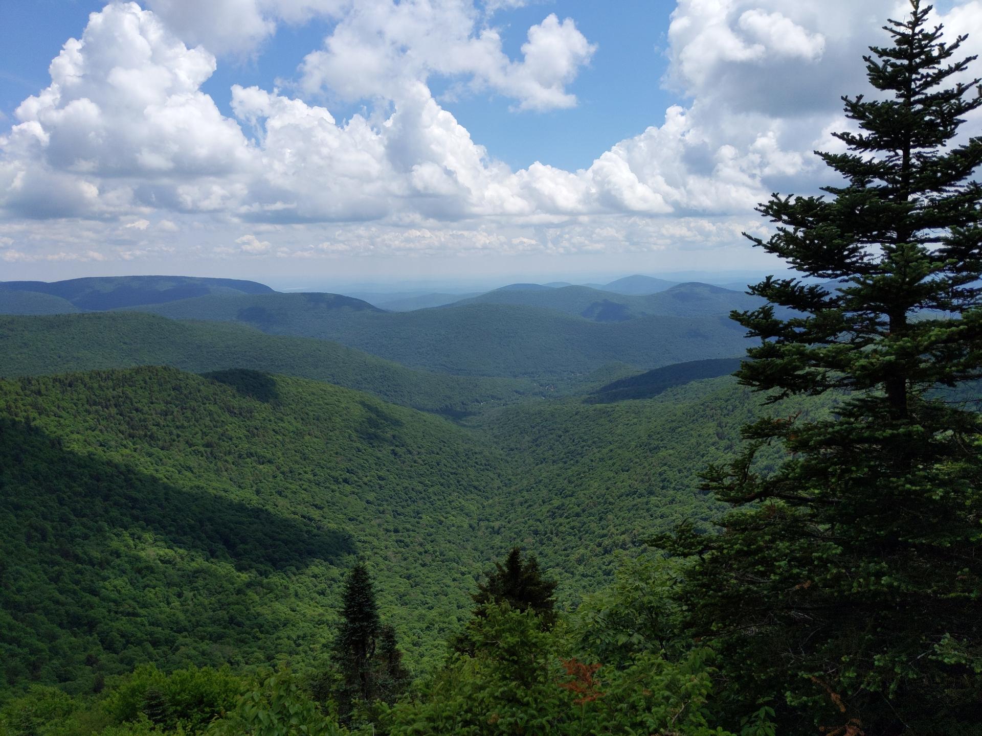 Vast green mountain landscape under a bright sky with fluffy white clouds.
