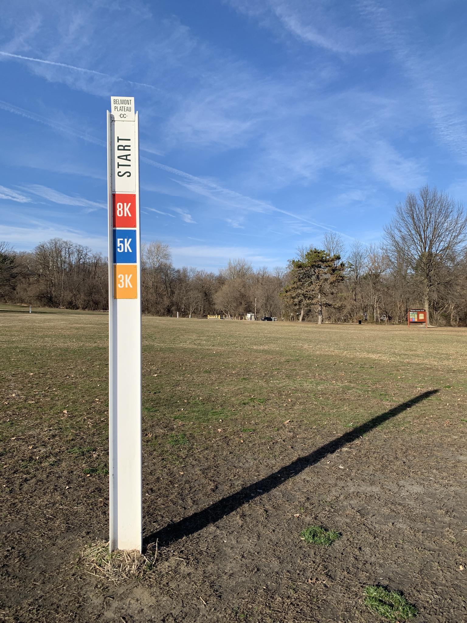 A white start post in a sunny, open grassy field under blue sky.