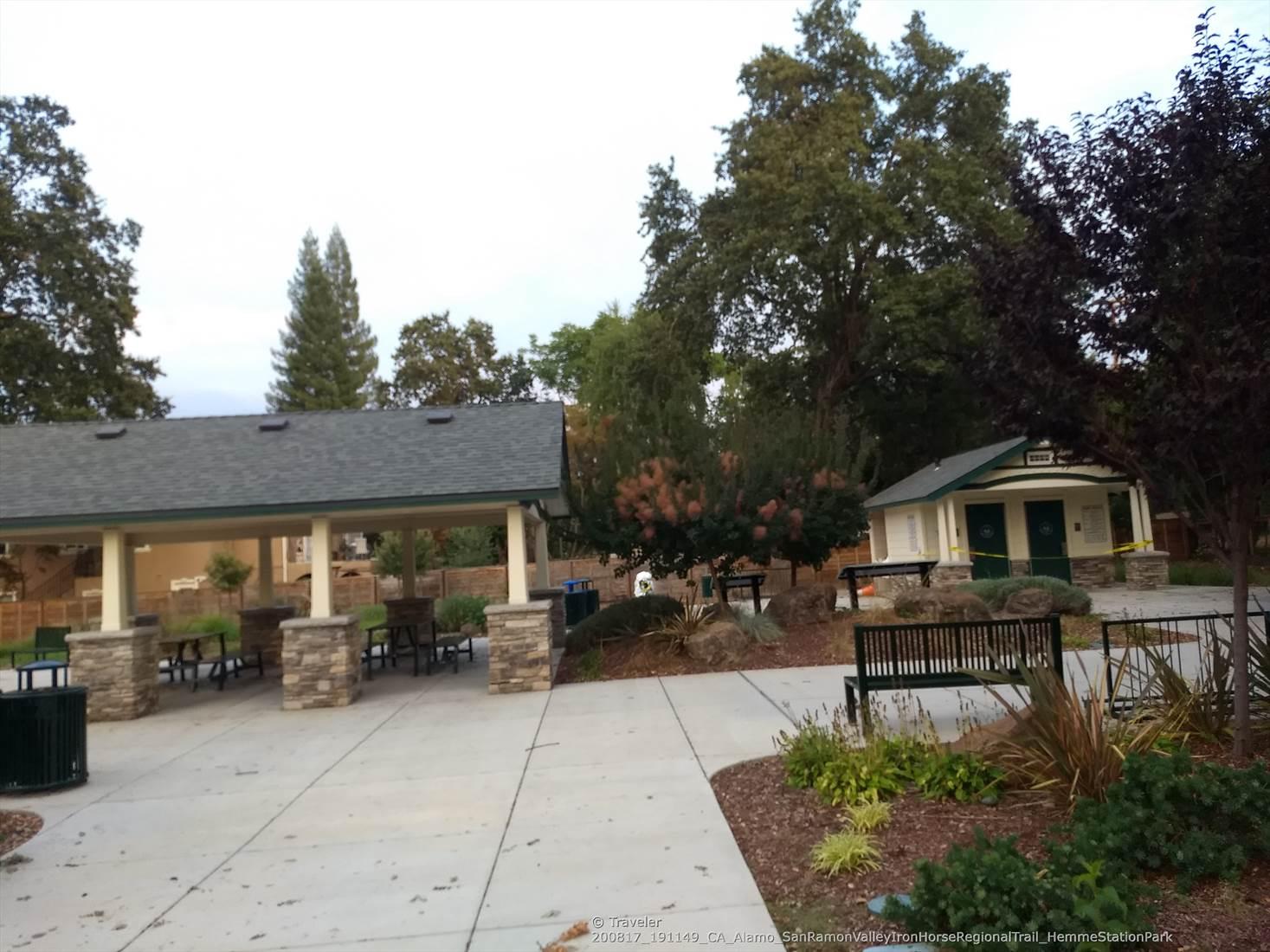 A park with a covered picnic area, small building, and benches under an overcast sky.