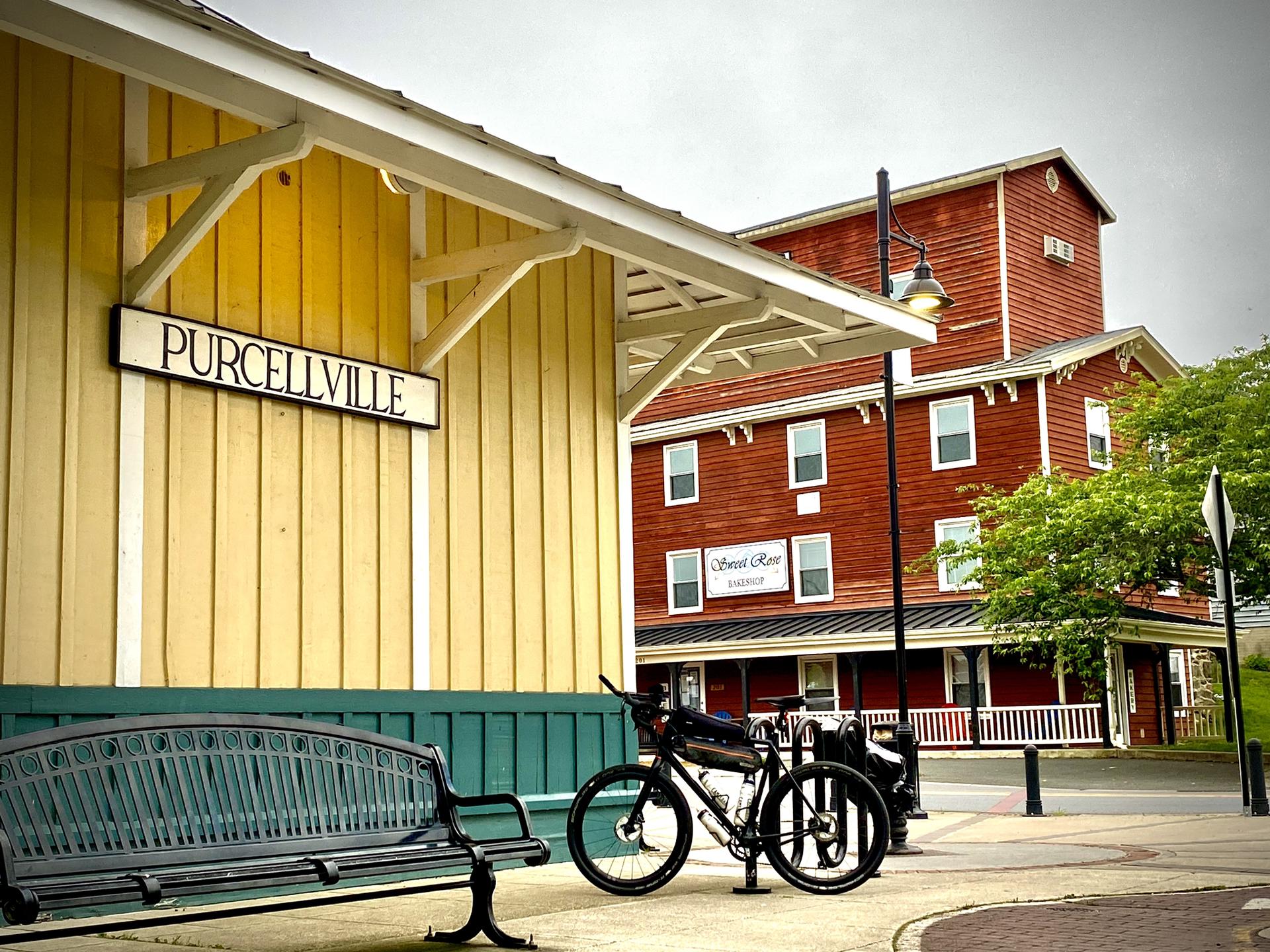 Yellow building with a sign, a bench, and a bicycle parked nearby.