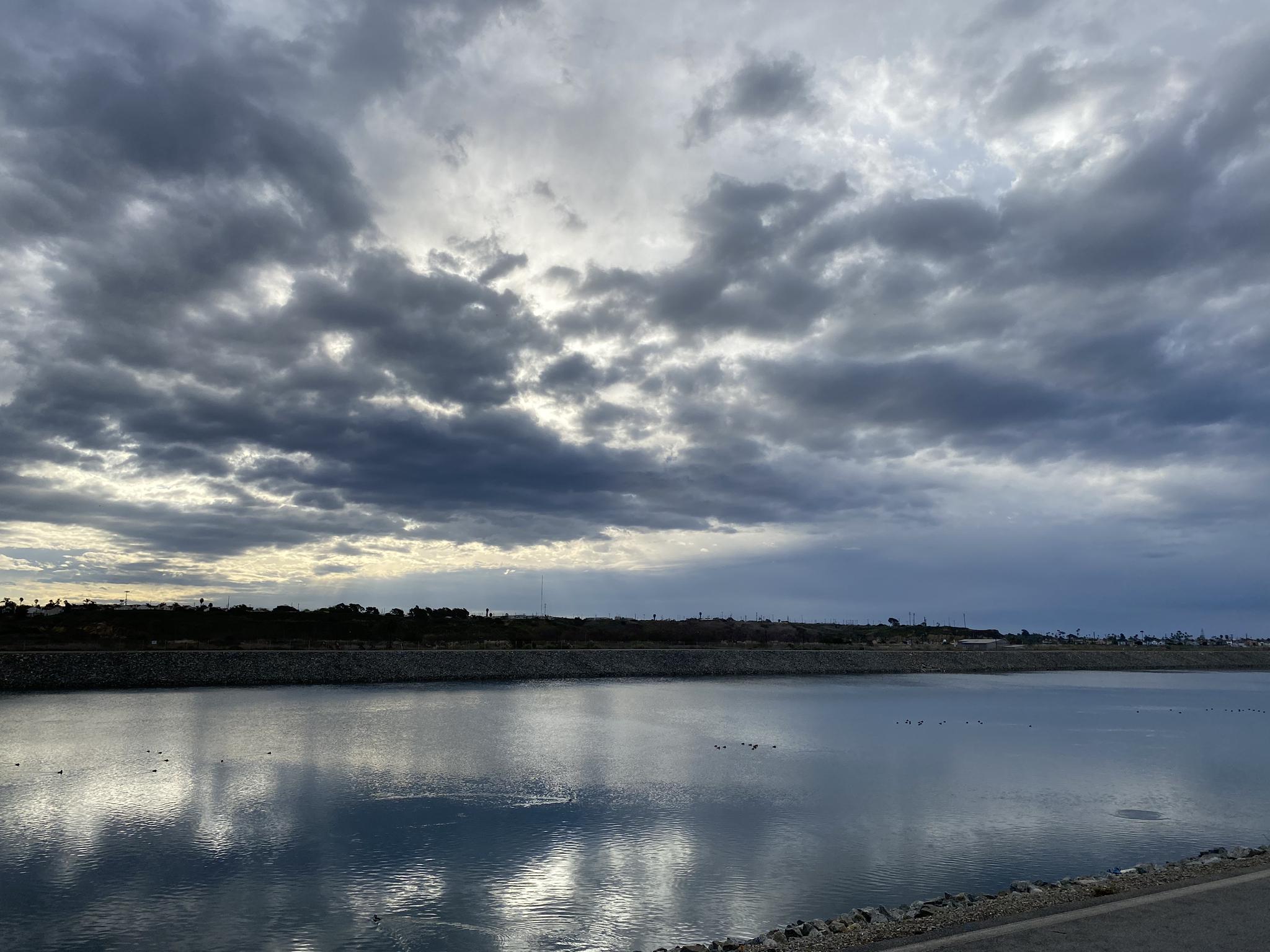 Overcast sky reflects on a wide, calm body of water with distant land.