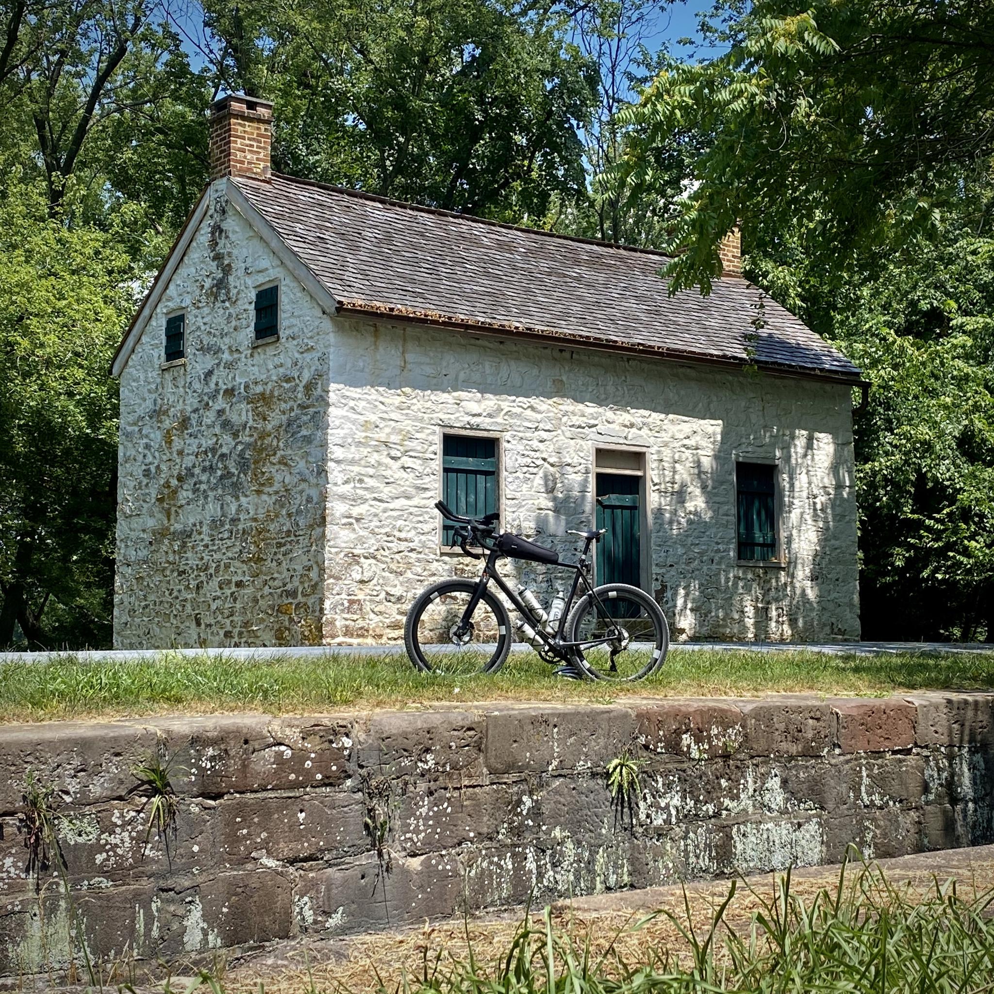 Stone house, bicycle parked on stone wall, surrounded by trees.