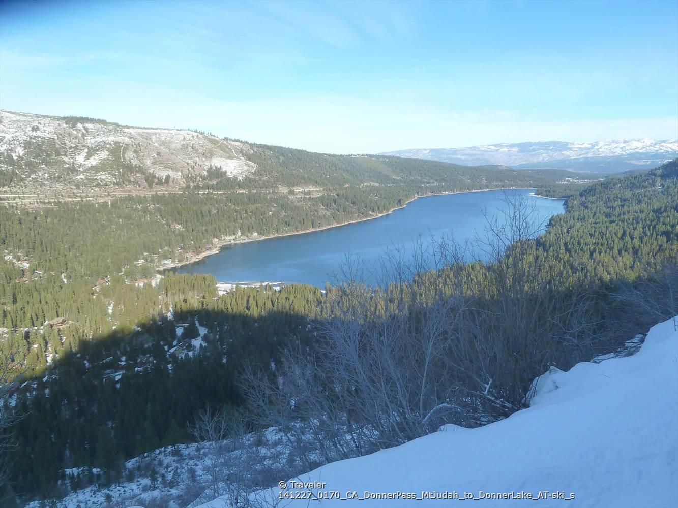 Wide blue lake surrounded by snow-dusted evergreen forests under a clear sky.