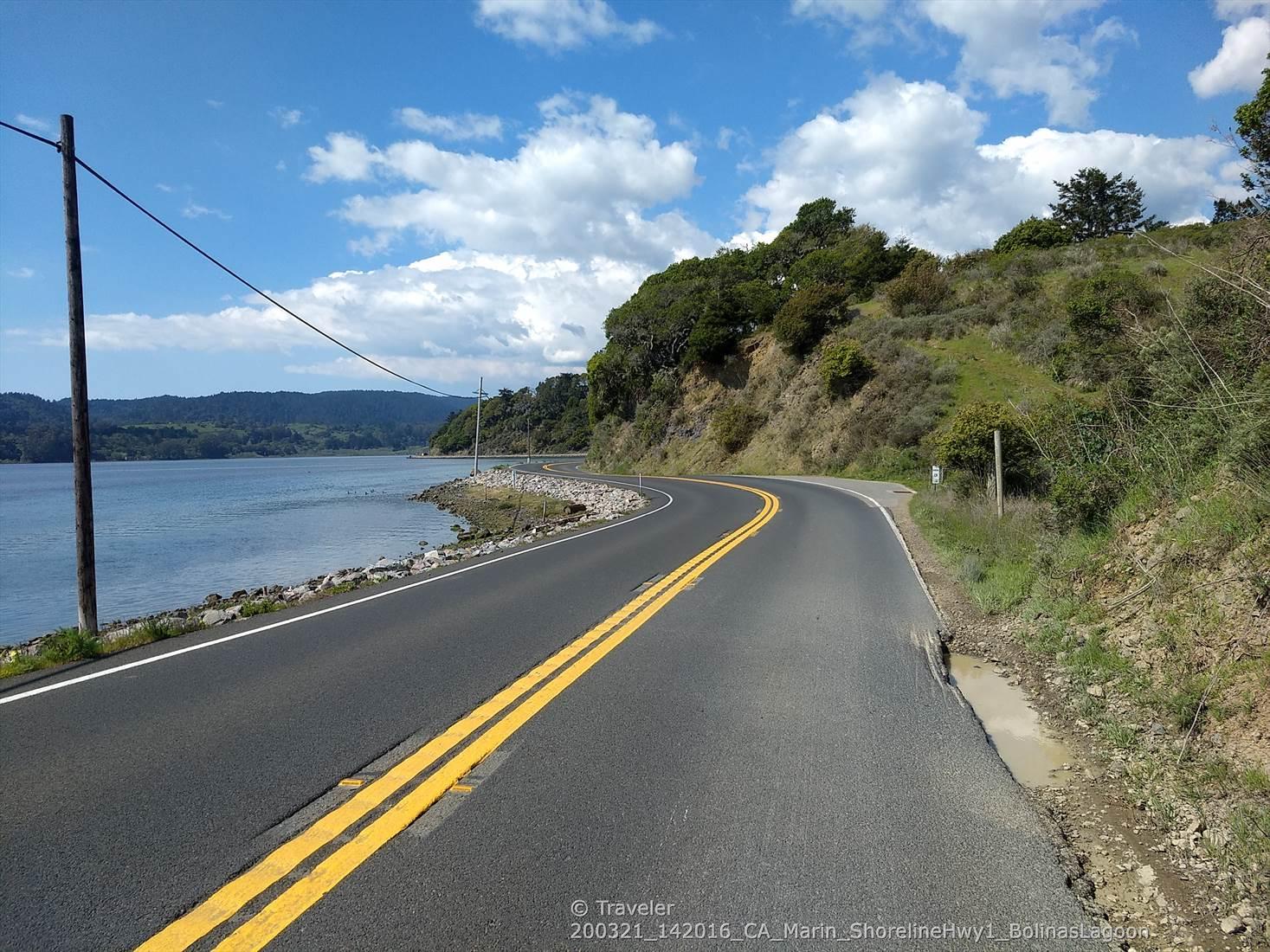 Curved paved road with yellow lines next to a large body of water.
