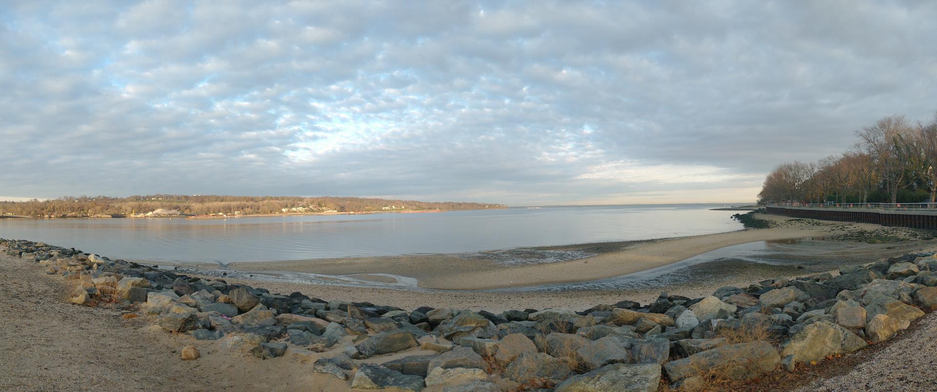 Panoramic view of a wide bay with rocky shore under cloudy sky.