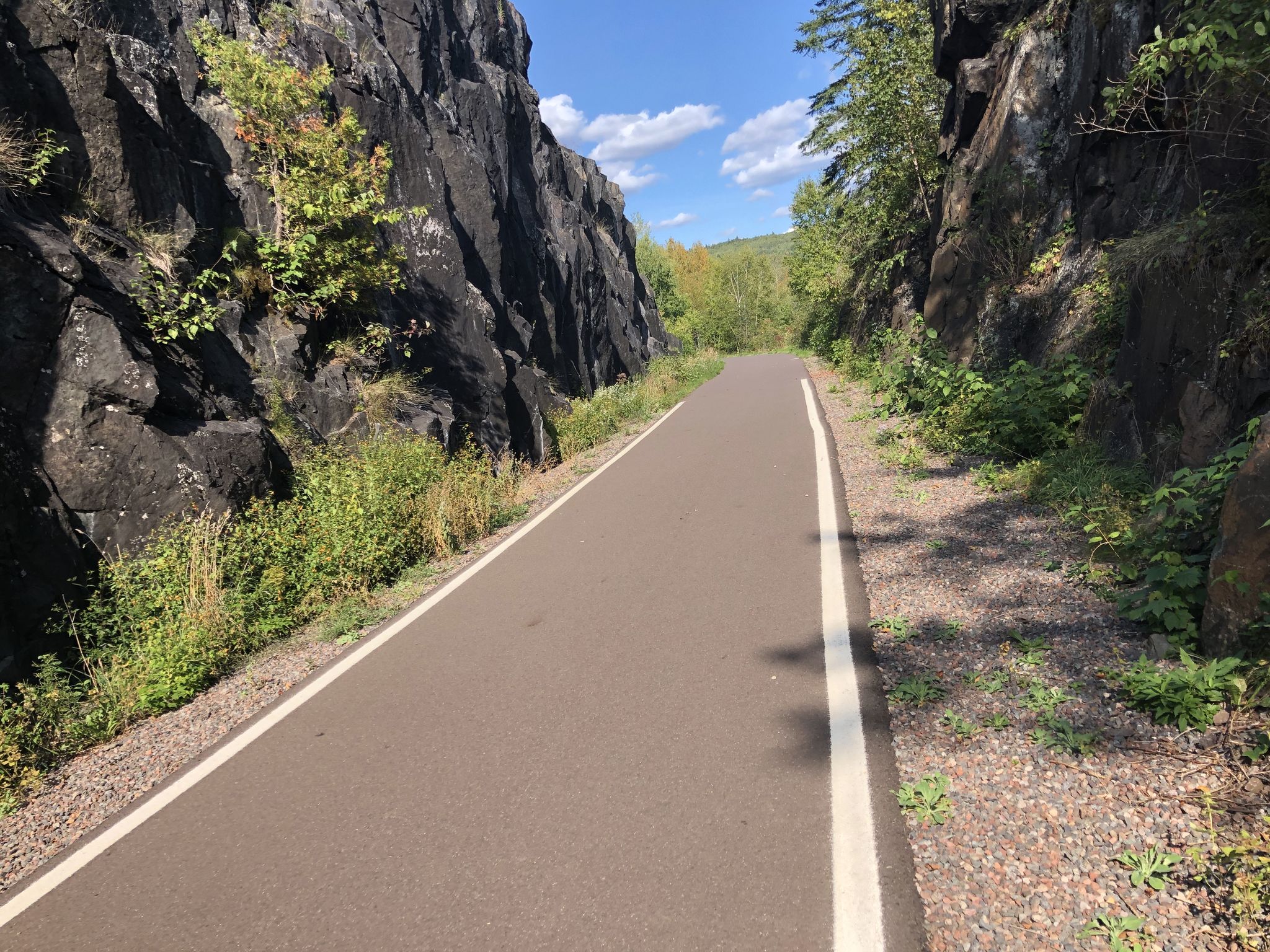 Paved path through a rock cut, under a bright blue sky. - Duluth Traverse and Lakewalk Loop