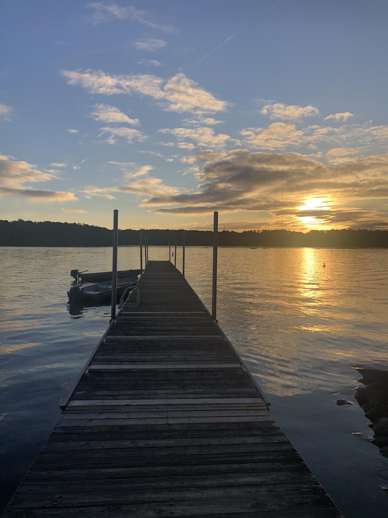 A wooden dock leads to a golden sunset over calm water.