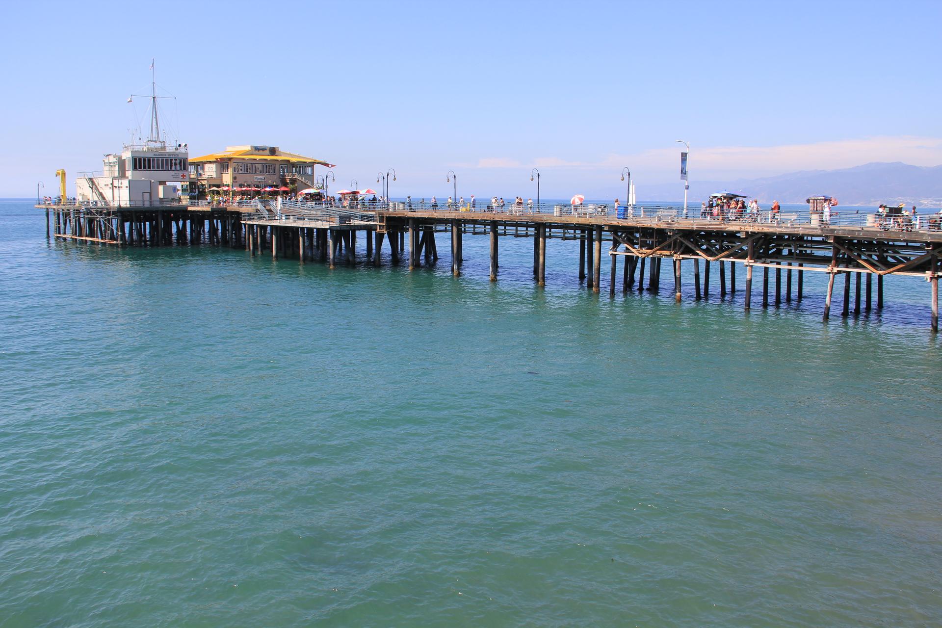 A long pier with buildings extends over blue ocean water under a clear sky.