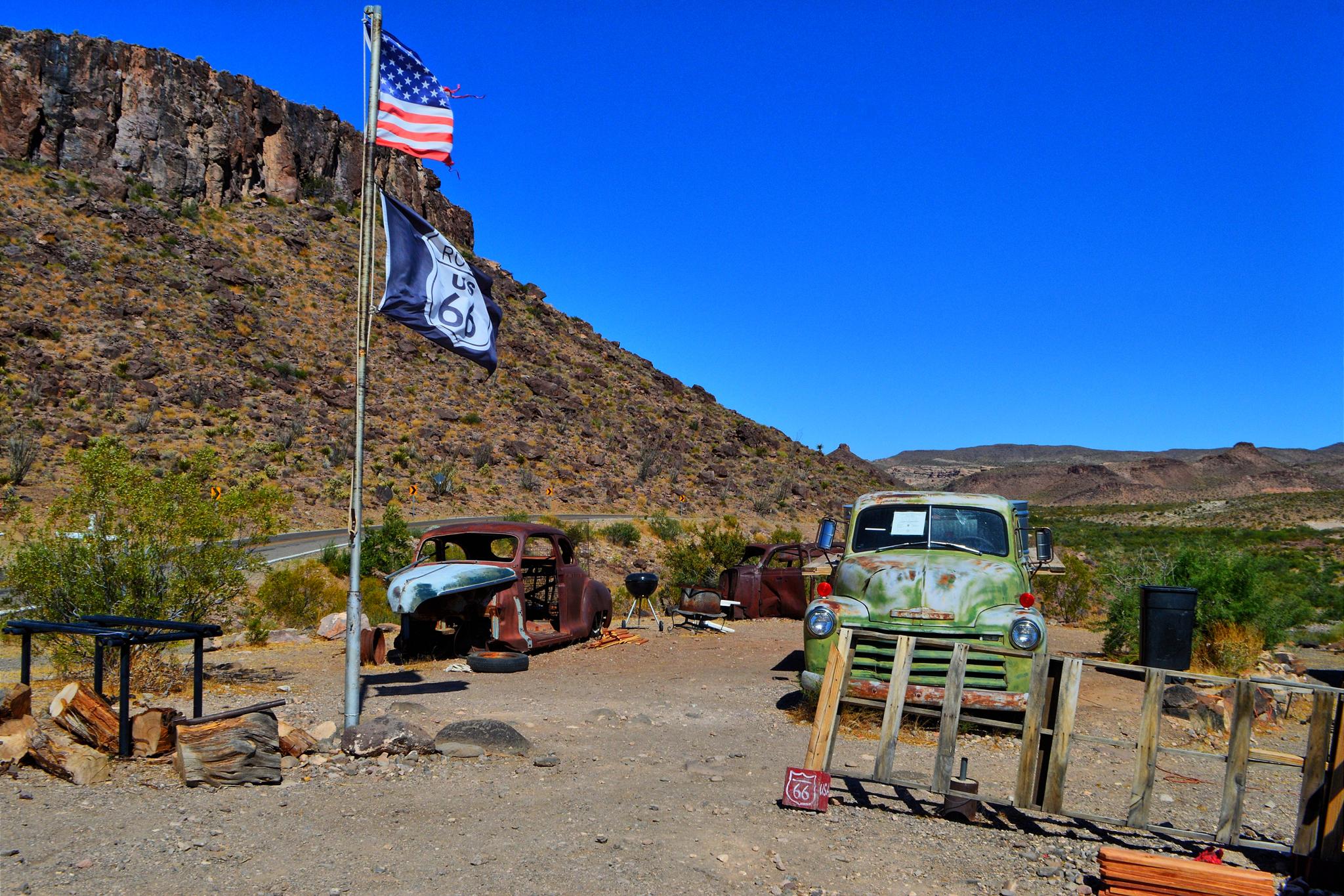 Old rusty cars and flags next to a rocky desert hill.