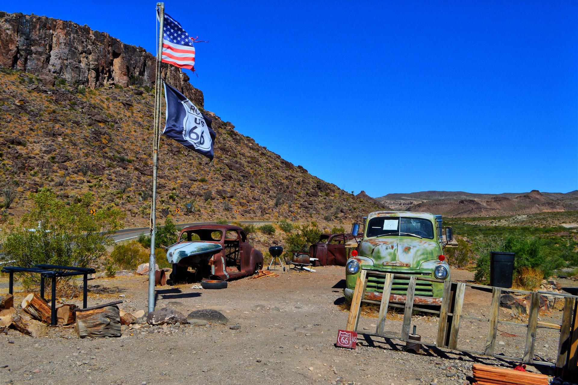 Old rusty cars and flags next to a rocky desert hill.