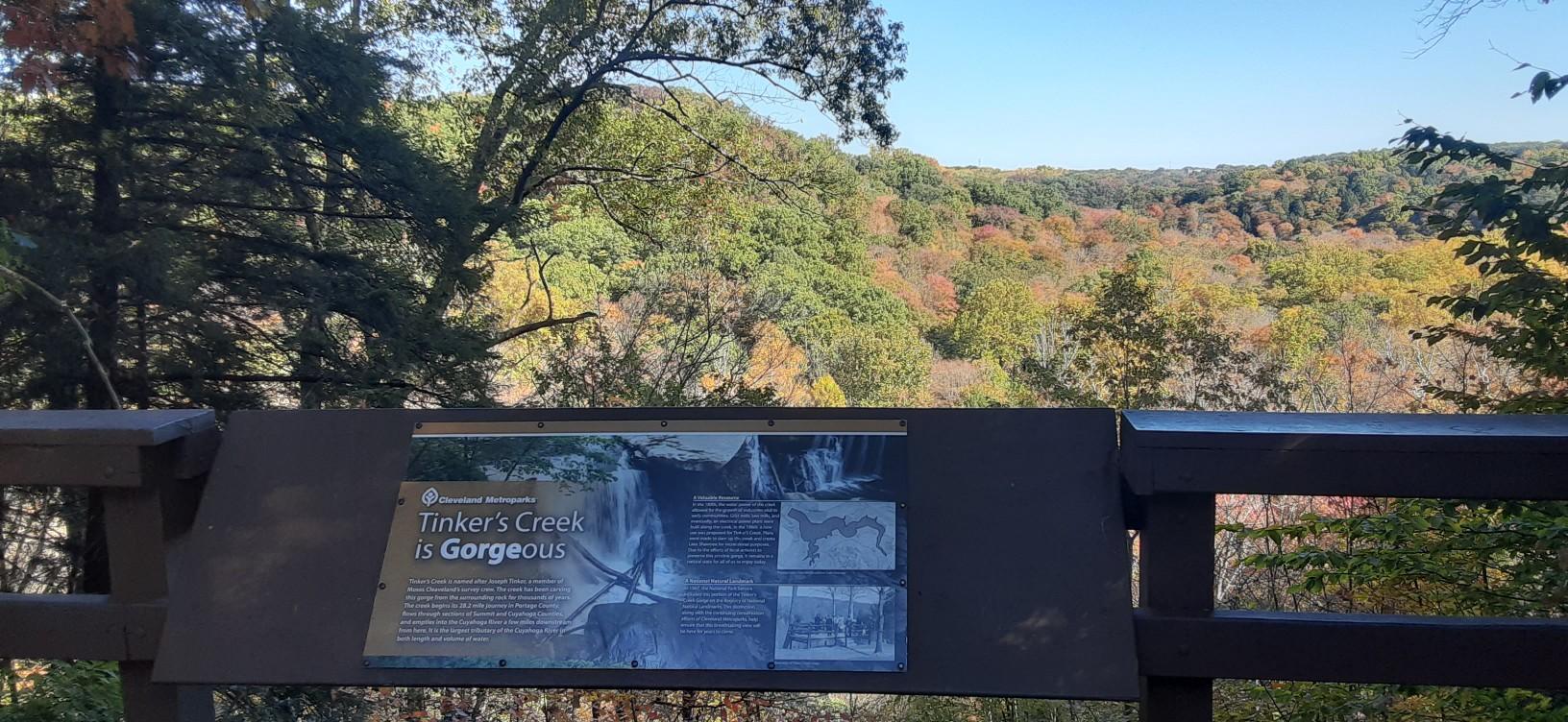 Information sign on a railing overlooking a vibrant autumn valley on a sunny day.