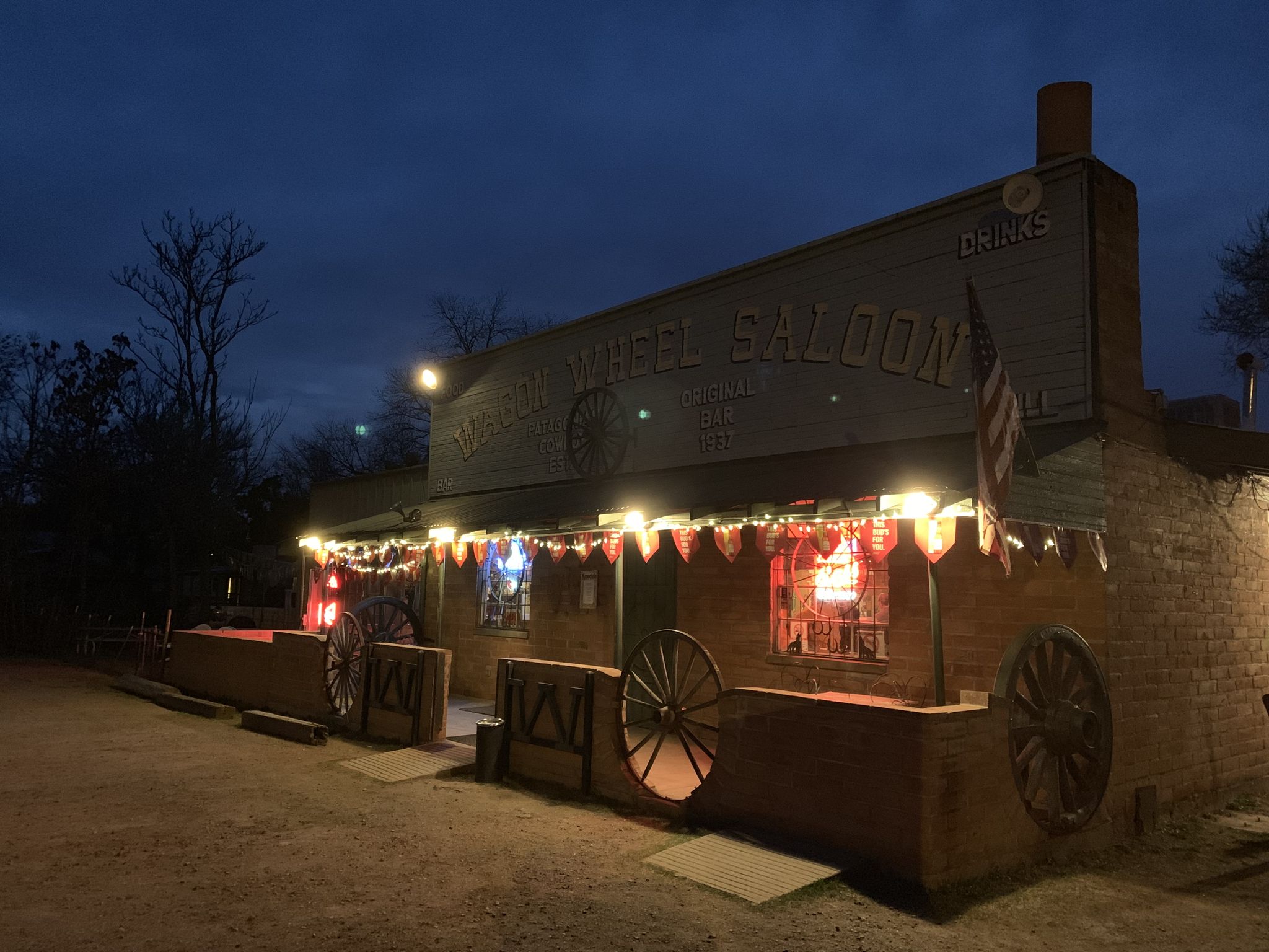 A lit-up saloon building with string lights and wagon wheels at night. - Nogales to Sonotia