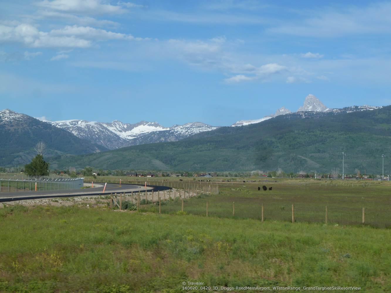 A curved road next to a green field, with distant snow-capped mountains.