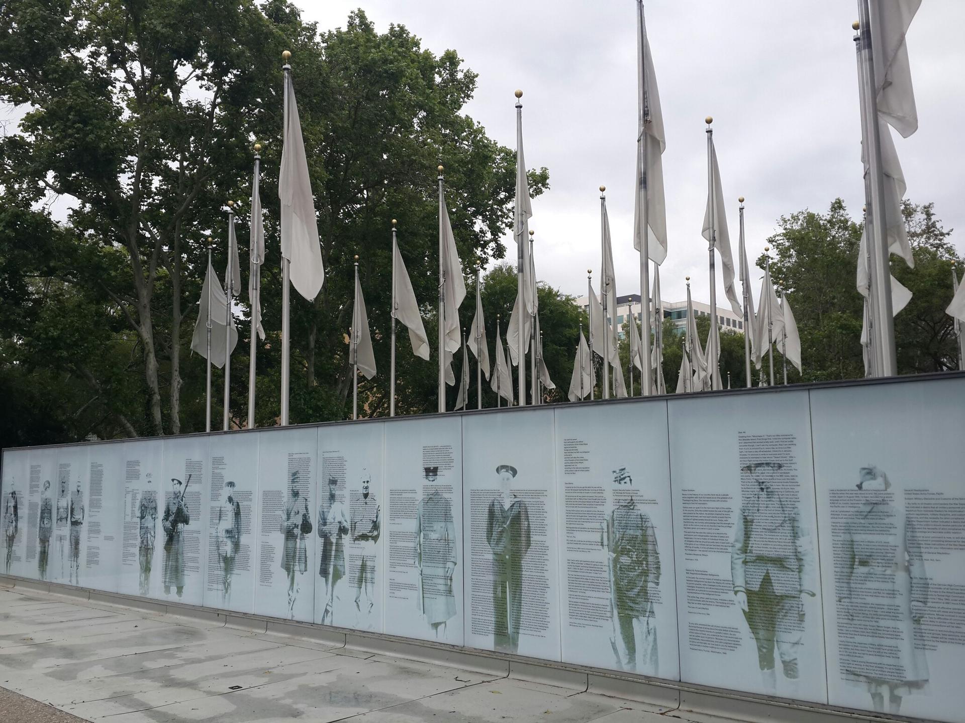 Wall with historical images and many white flags under an overcast sky.