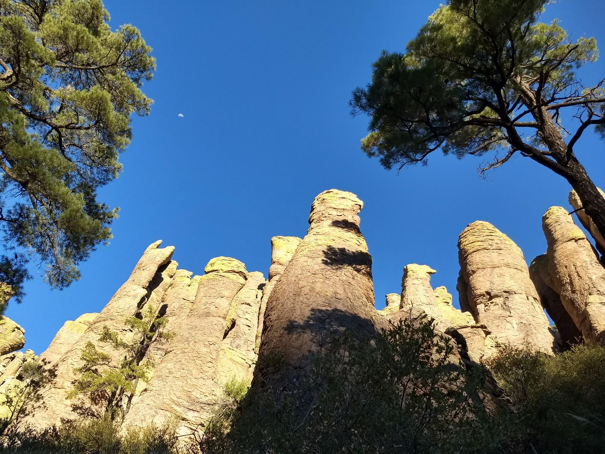 Towering rock formations reaching towards a deep blue sky, framed by trees.