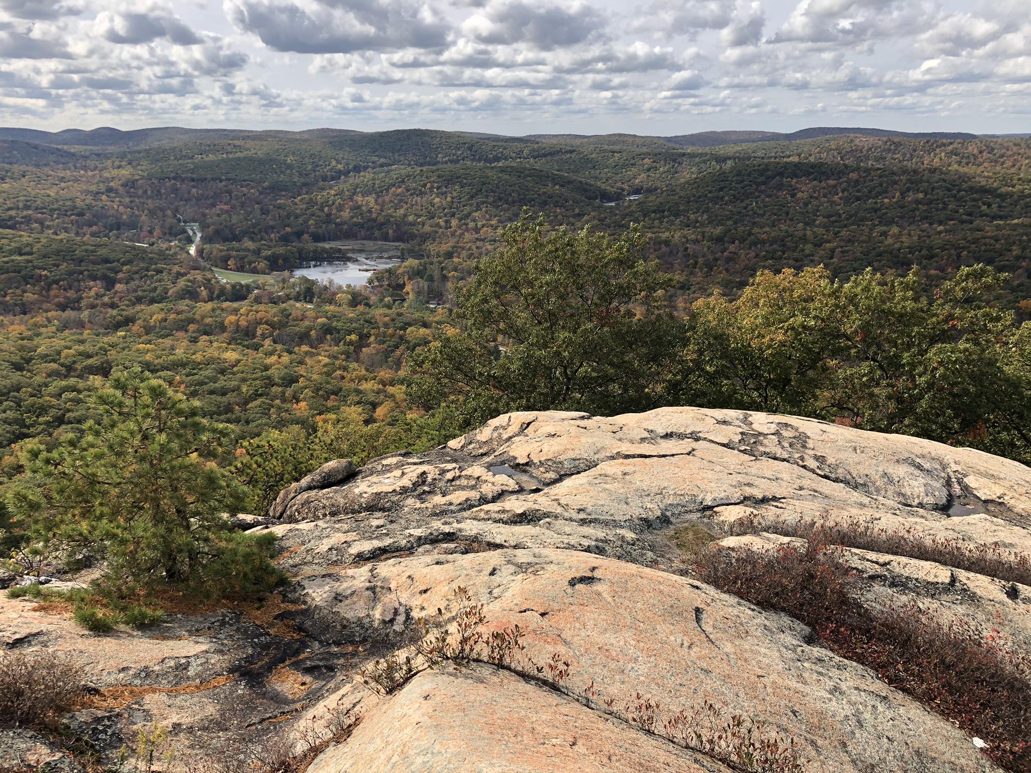 Rocky overlook revealing a lake surrounded by autumn-colored forests under a cloudy sky.