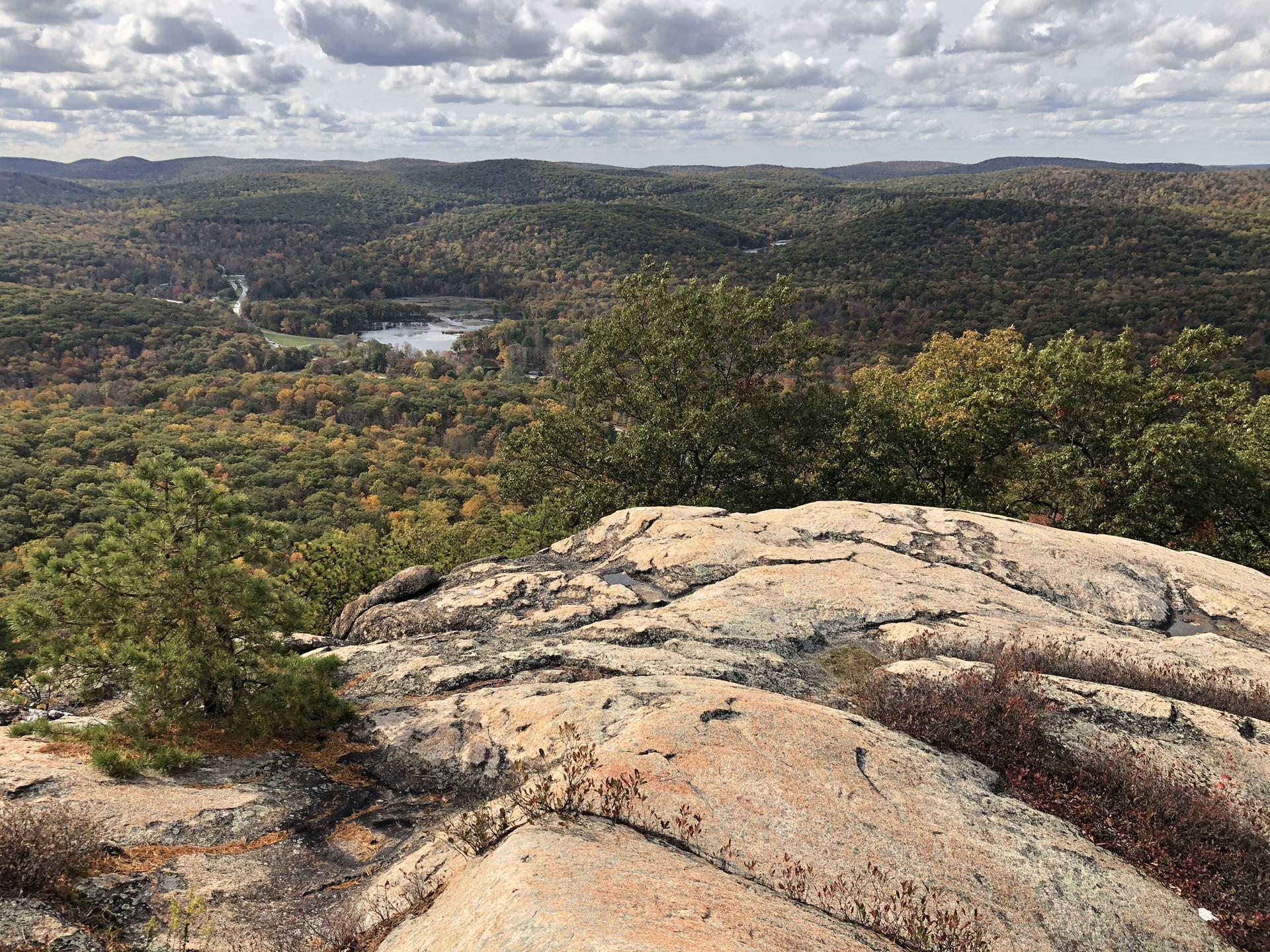 Rocky overlook revealing a lake surrounded by autumn-colored forests under a cloudy sky.