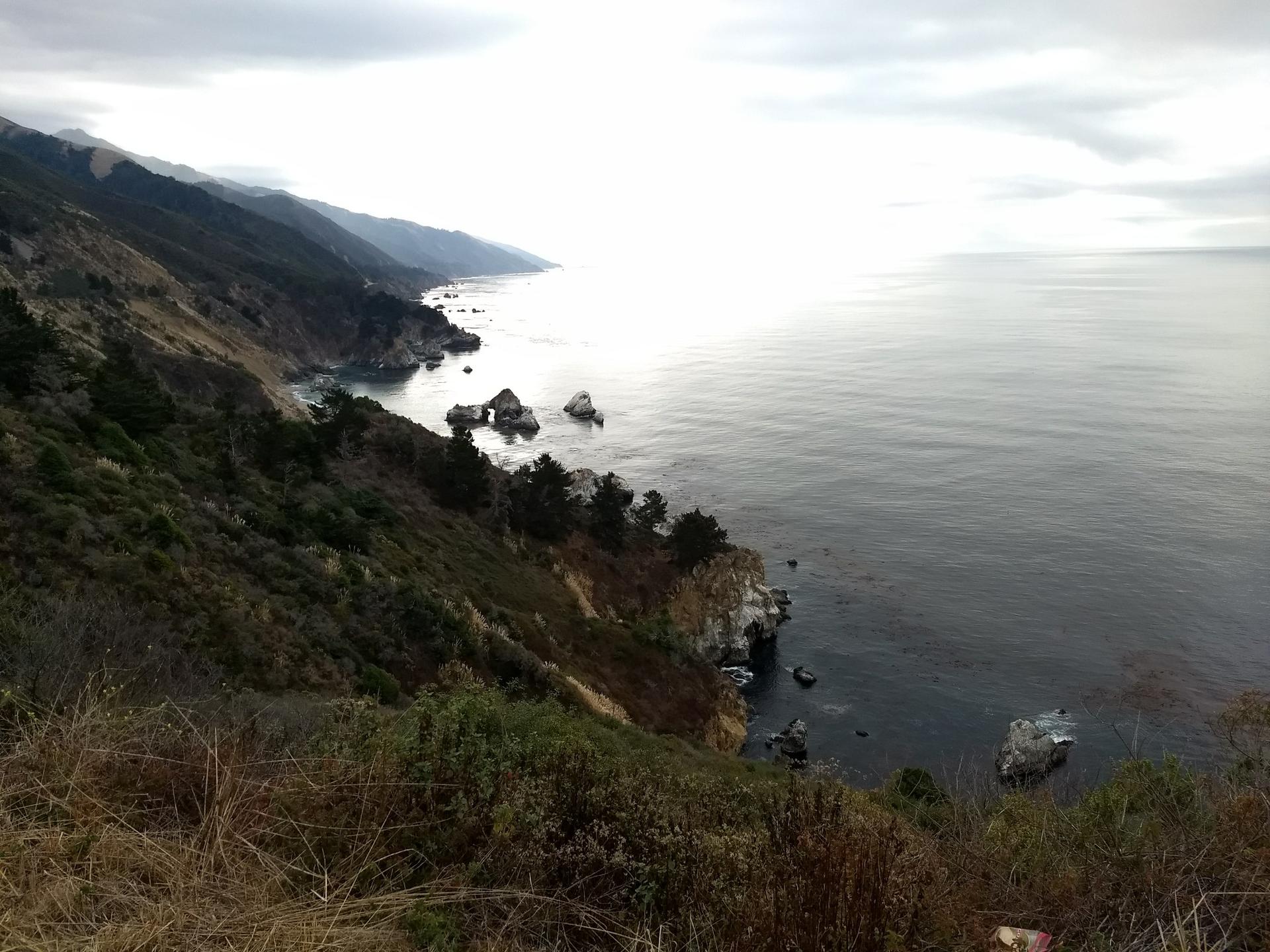 Overcast view of a rugged coastline with dark ocean and distant mountains.