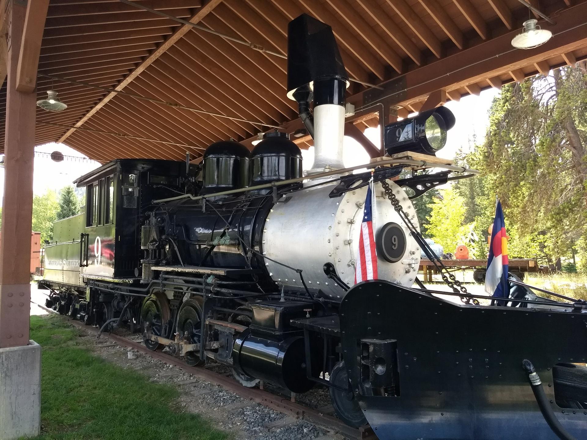 Historic black and silver train engine with flags under a wooden shelter.