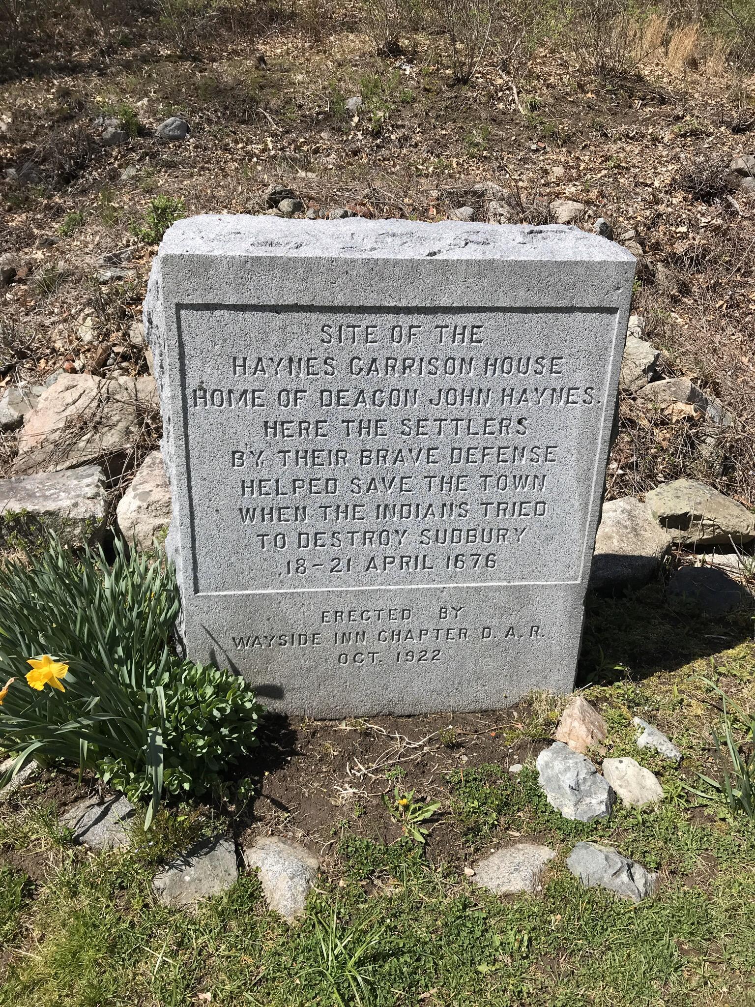 A weathered stone monument on a sunny grassy slope with small plants.