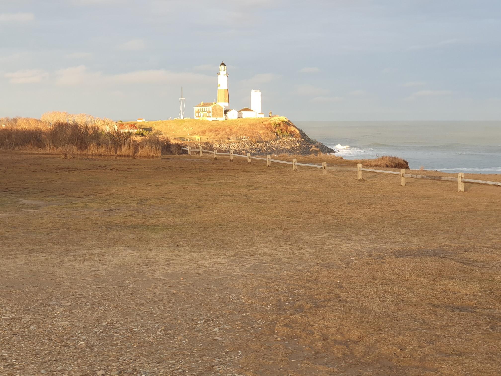 Distant lighthouse on a sunlit cliff overlooking the ocean, with a grassy foreground.