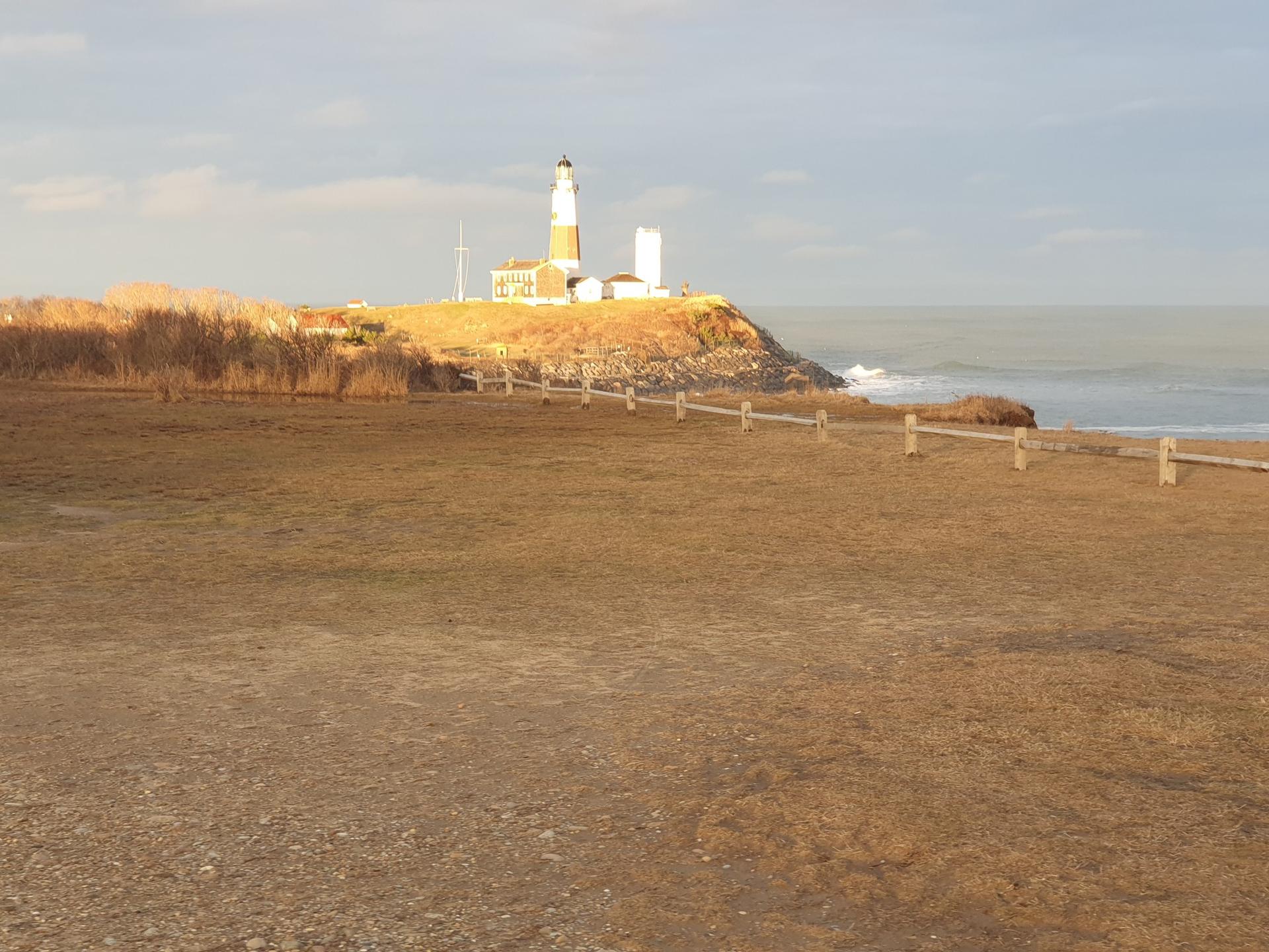 Distant lighthouse on a sunlit cliff overlooking the ocean, with a grassy foreground.