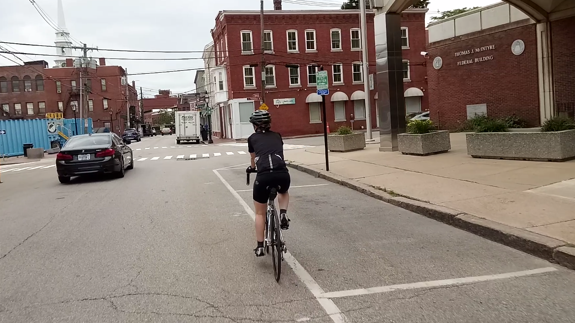 Cyclist on an urban street with brick buildings under an overcast sky.